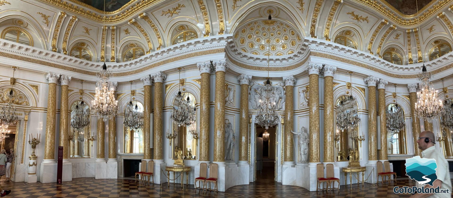 a ceremonial ballroom in the castle, a checkerboard floor, crystal chandeliers, yellow columns with Corinthian capitals, Roman style sculptures, yellow, white and golden ornaments dominate
