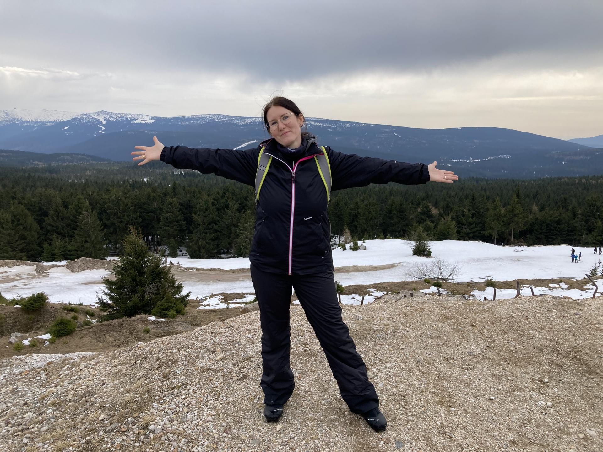 A woman standing on a hill, behind her is a skyline of mountains