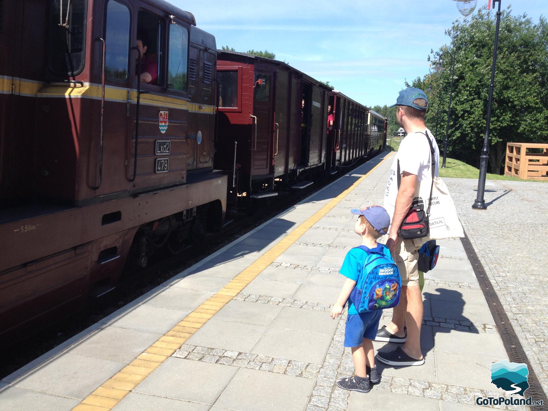 Two boys and a man watching a train arriving at the station