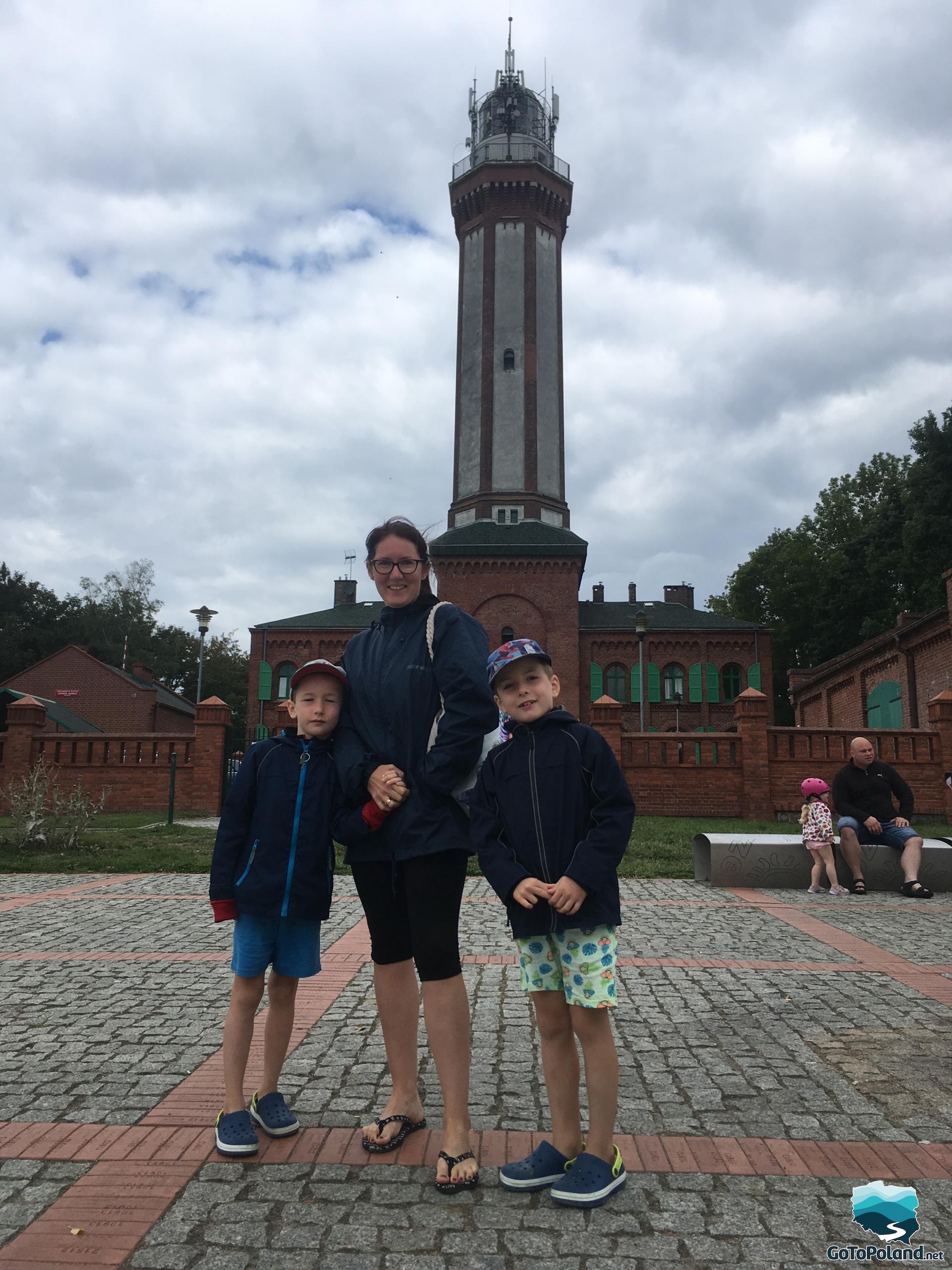 a woman and two boys are standing in front of a lighthouse 