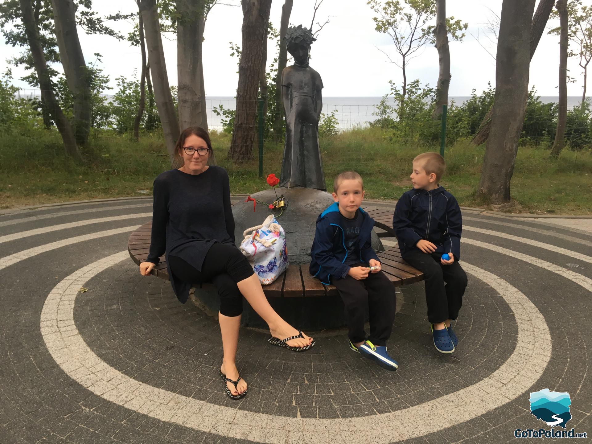 a woman and two boys sitting by the statue of the little prince