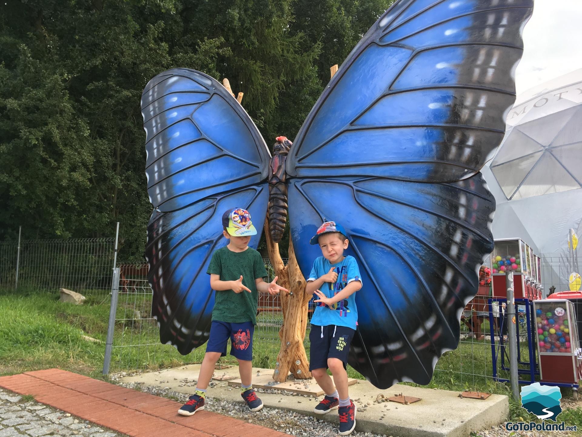two boys in front of a big blue model of butterfly