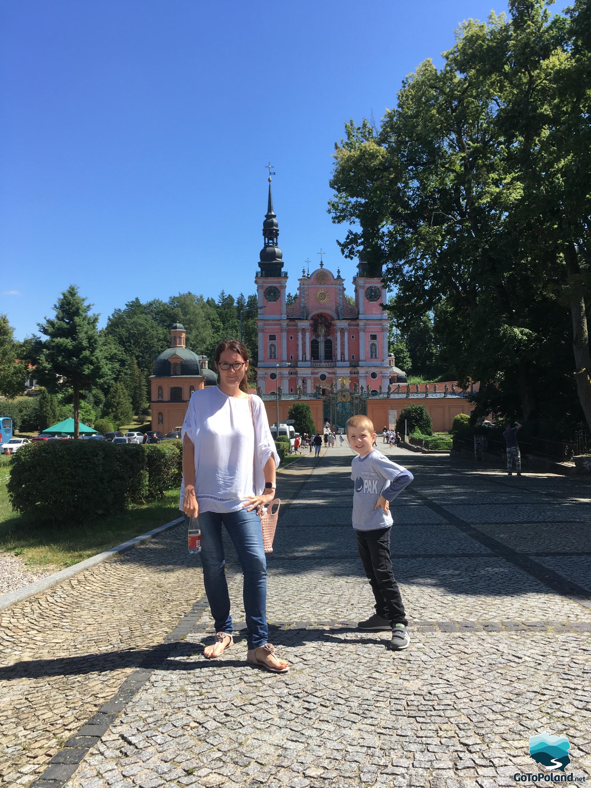 a woman and a child standing in front of a sanctuary, the building of the sanctuary is pink with two spires