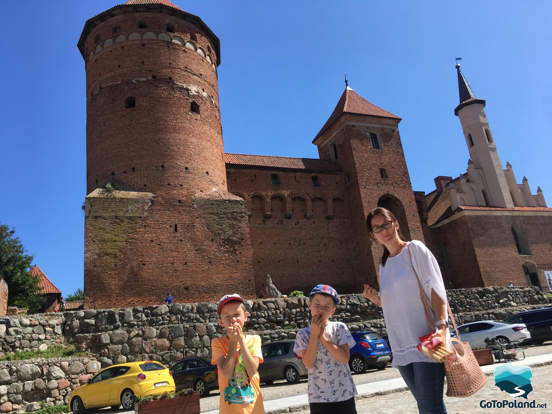 a brick castle, in front of it there is a woman and two boys