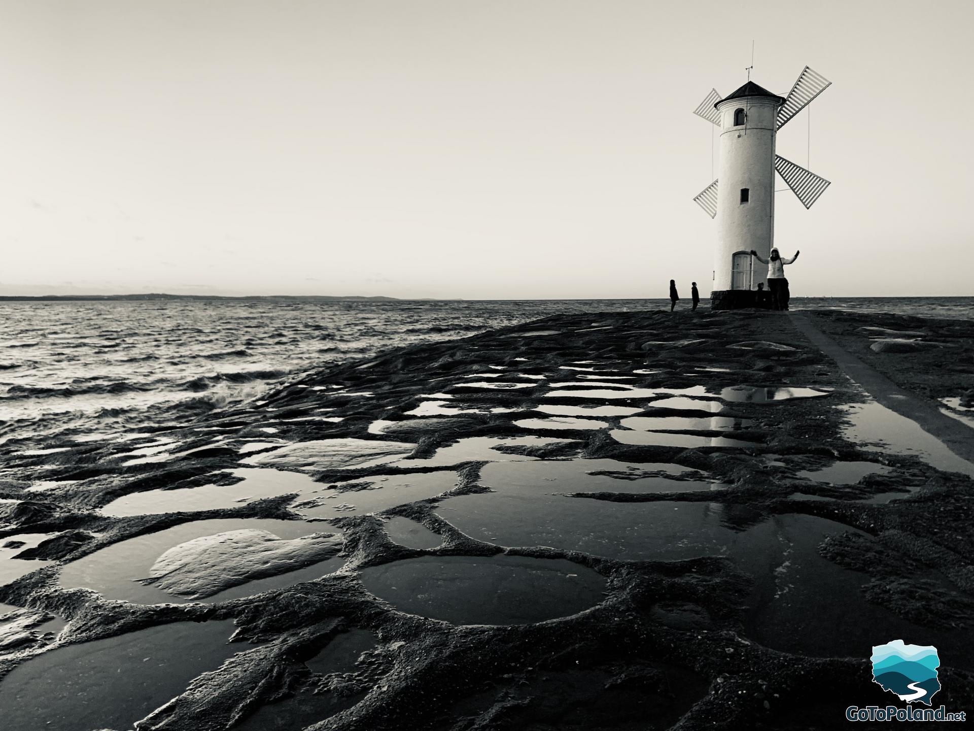a white windmill at the end of the breakwater, black and white picture