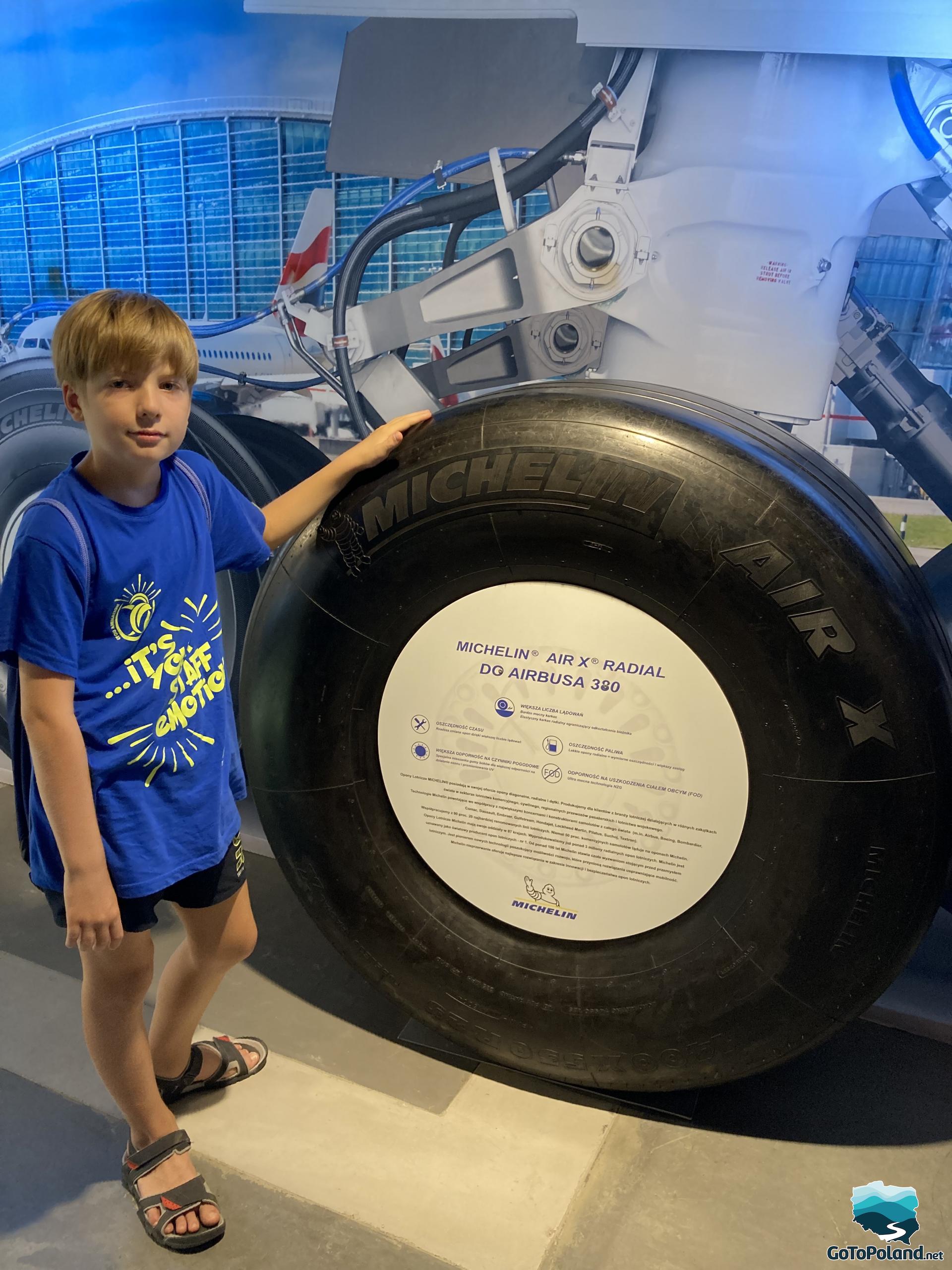 a boy is standing in front of a huge tire made for Airbus aircraft