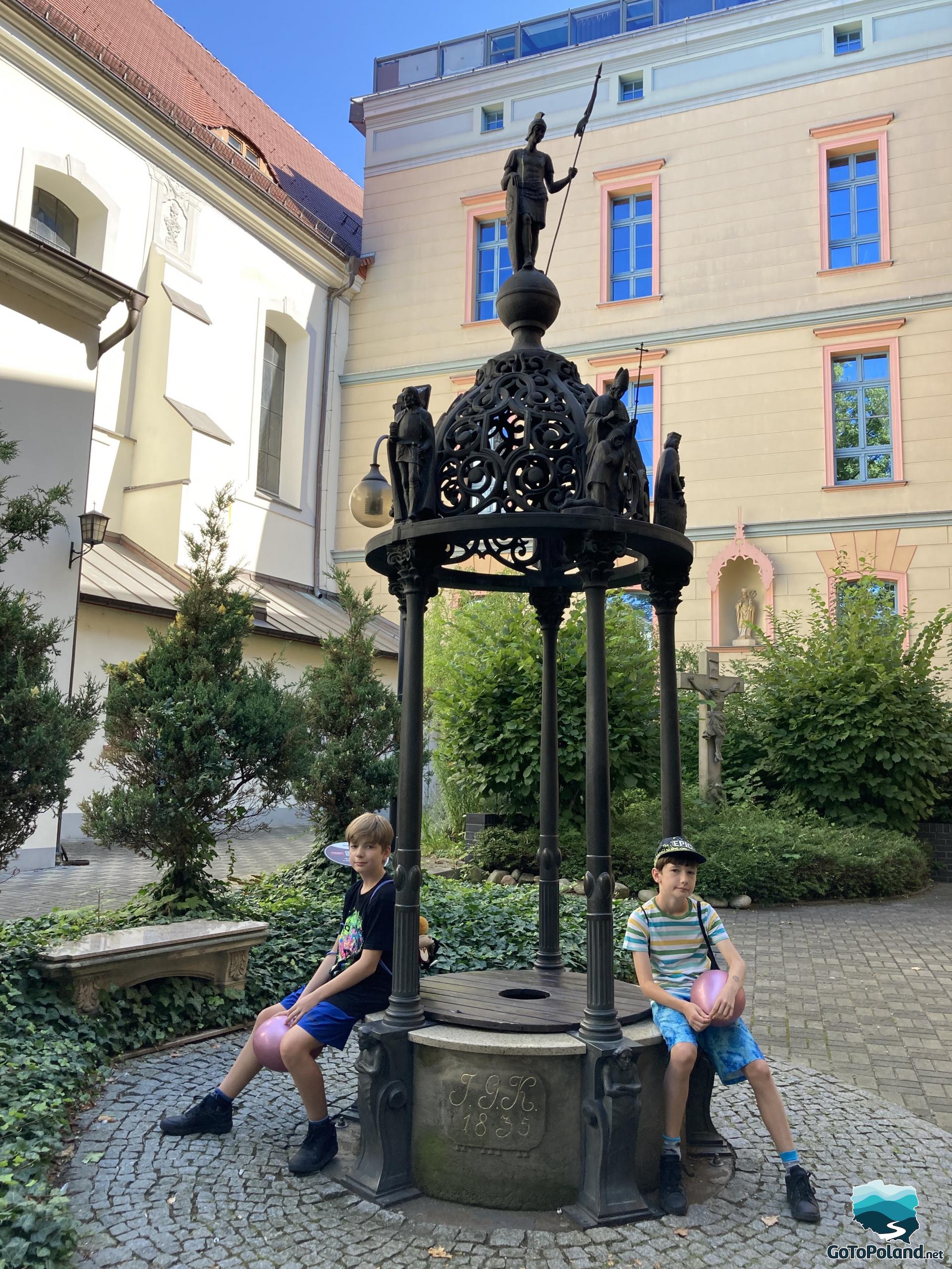 two boys sitting by an openwork well