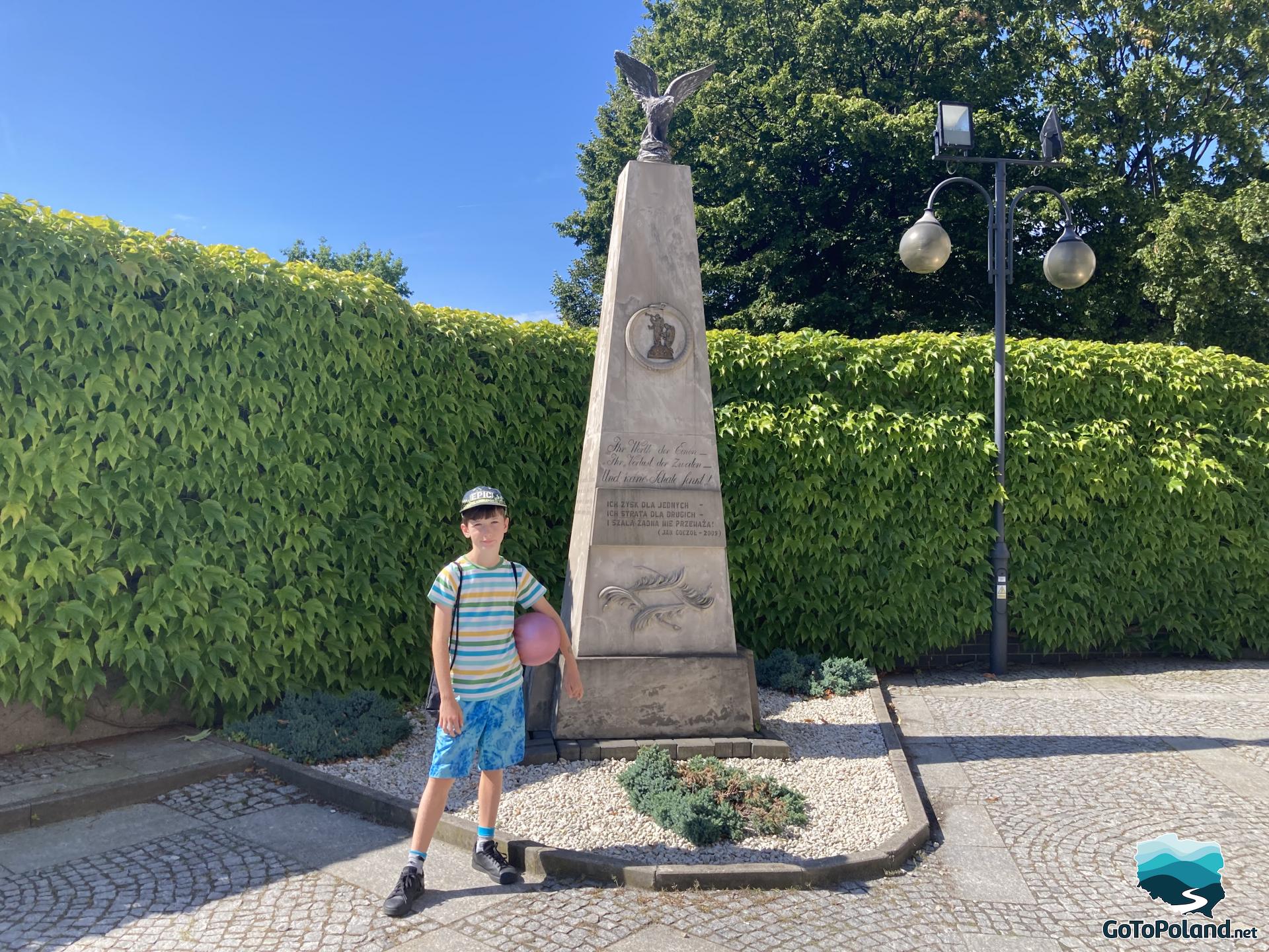 a boy standing next to a monument, at the top of which there is a statue of an eagle