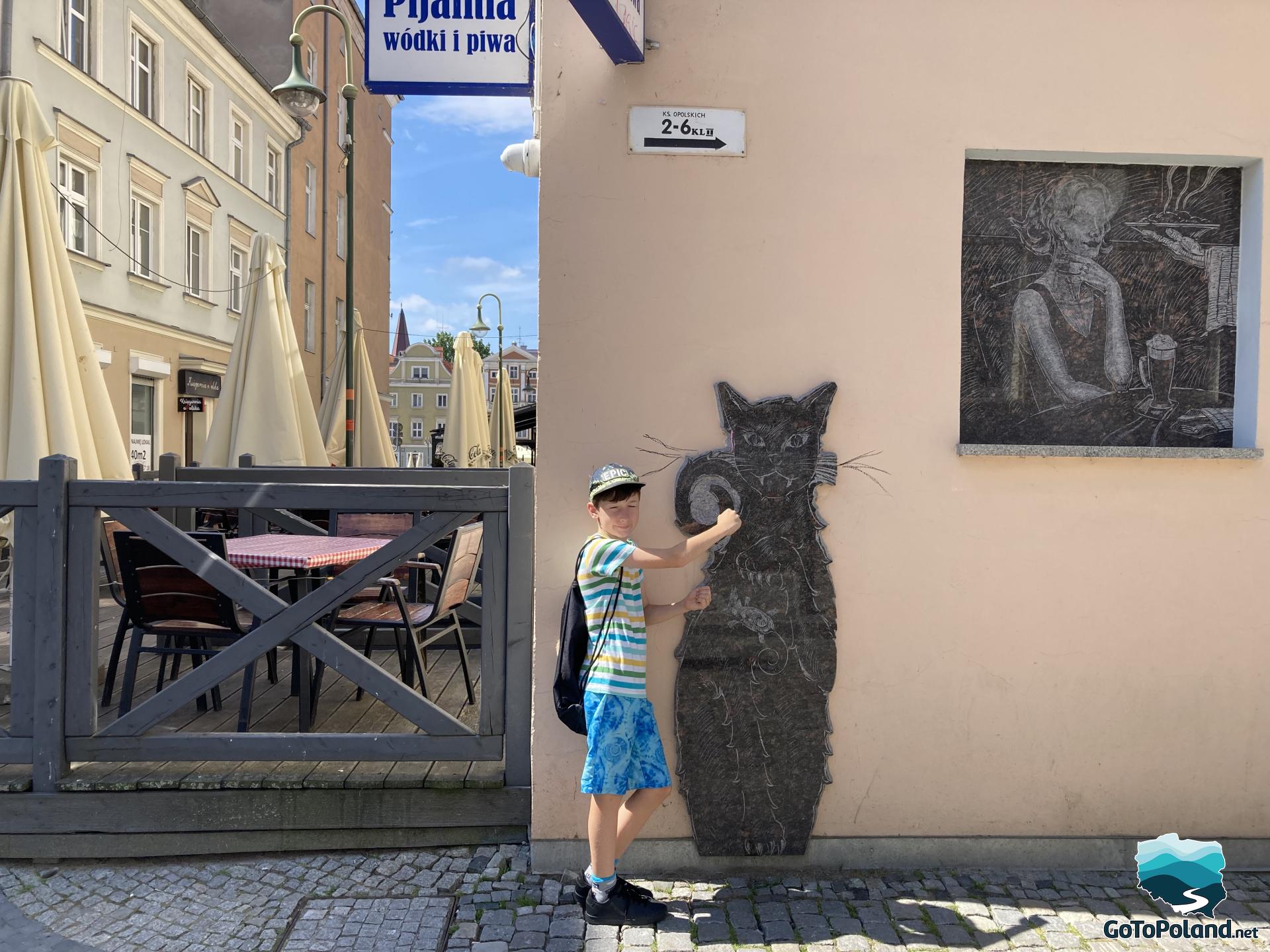 a boy next to a cat mosaic incorporated into the wall of a building