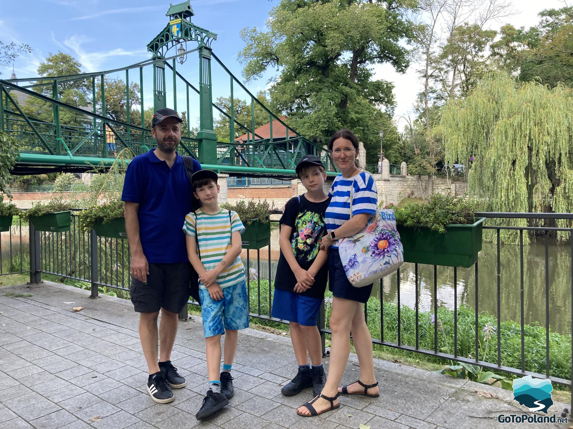 a family standing next to the river and a green bridge 