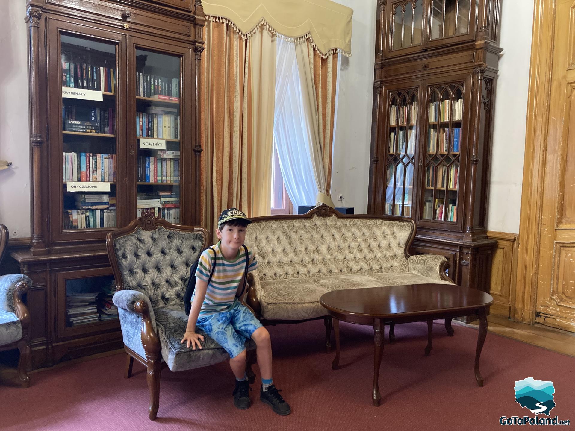 a boy is sitting in an armchair next to the table in a library