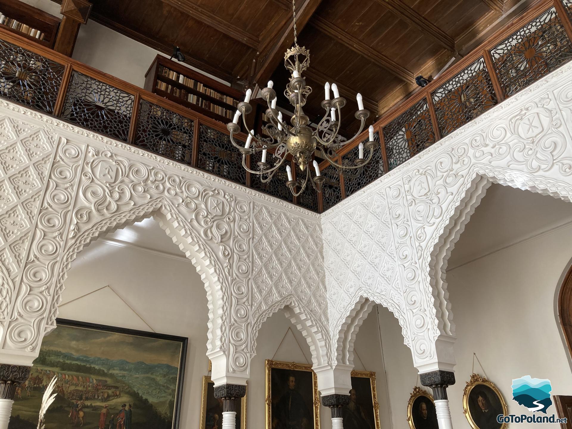 Arabic, white column tops, shelves with books on the first floor, hanging chandelier