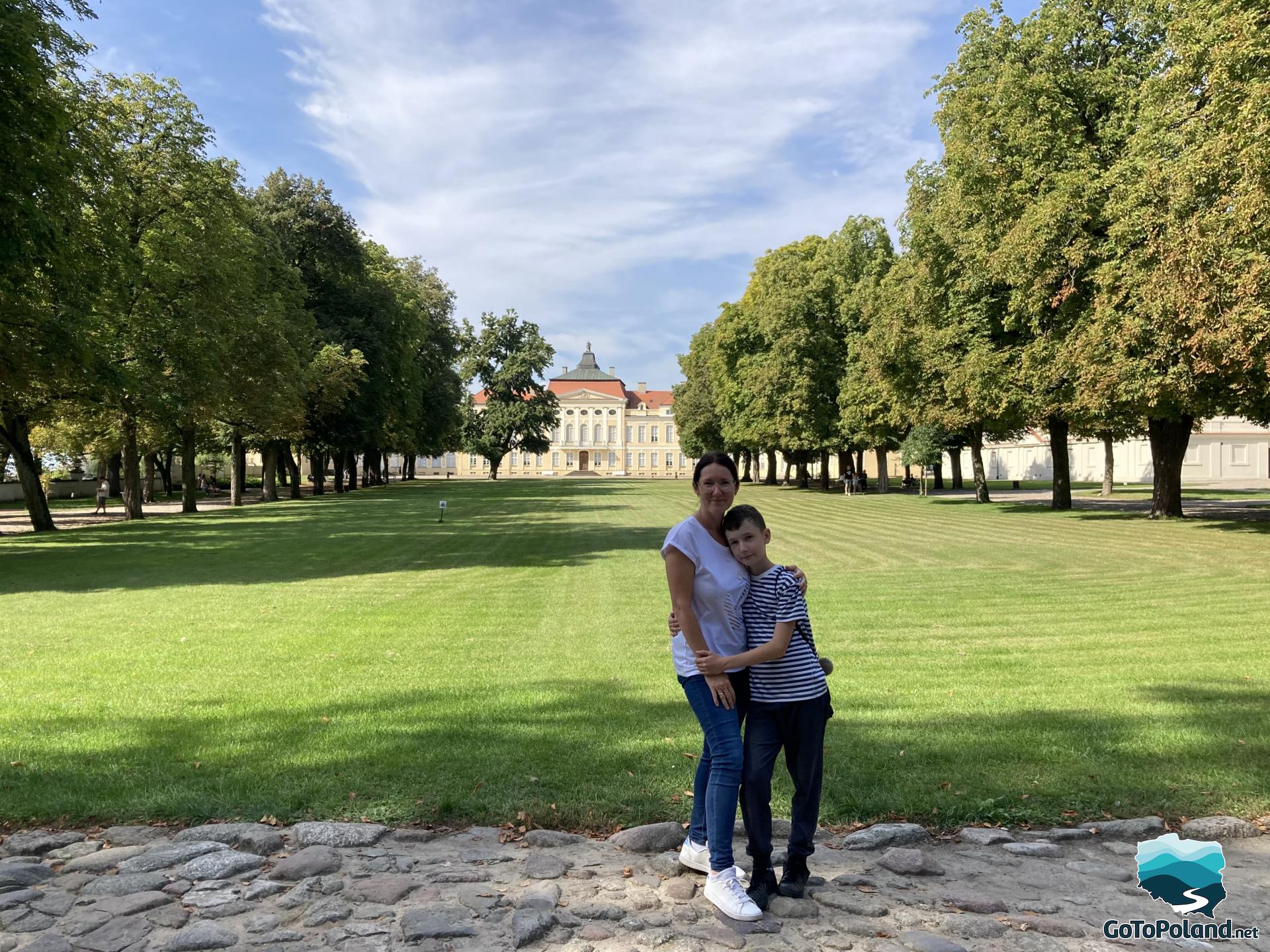 woman and boy hug, a palace looms in the background 