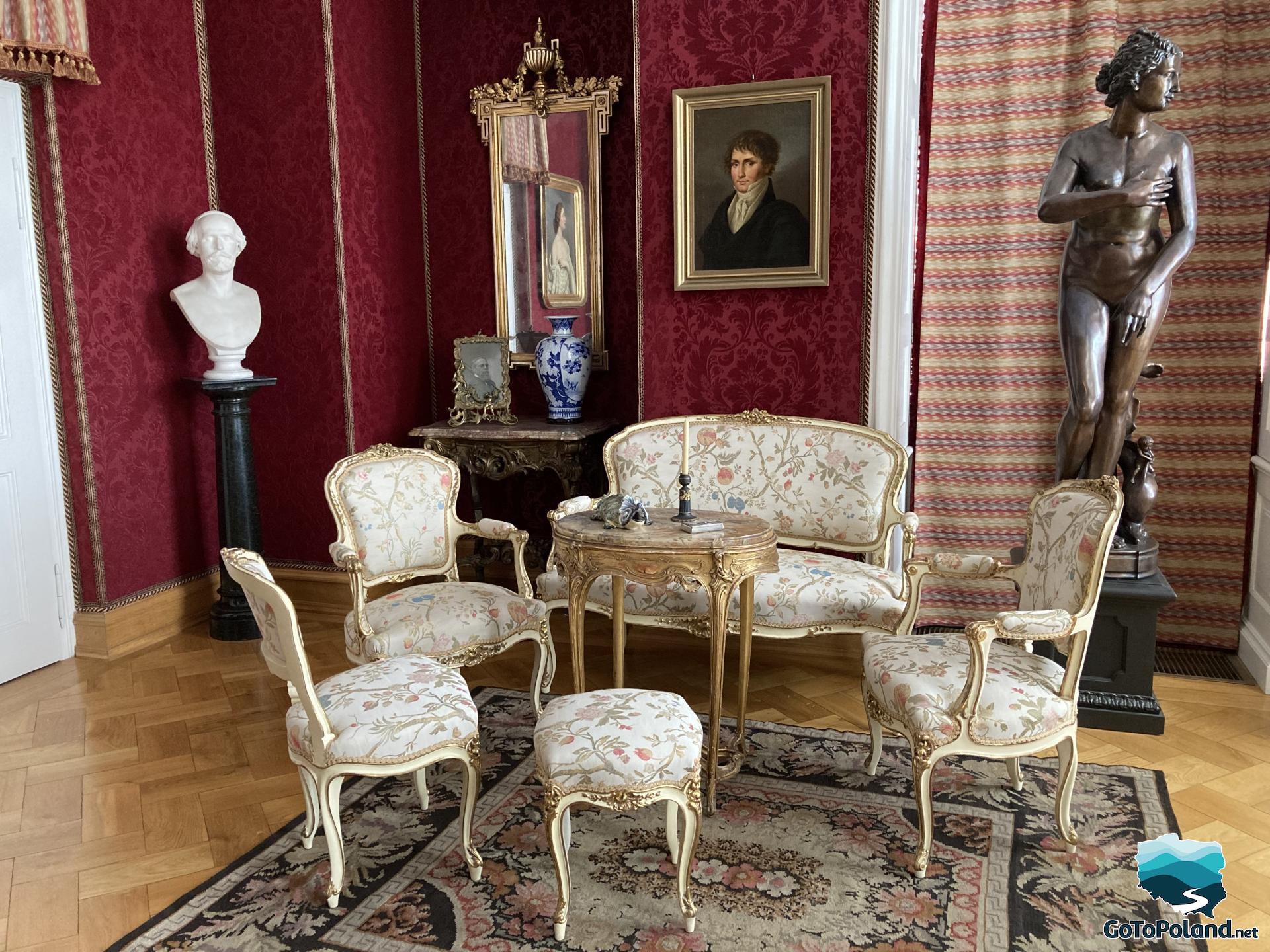 a room with red wallpaper, there are two sculptures, three armchairs and a small sofa