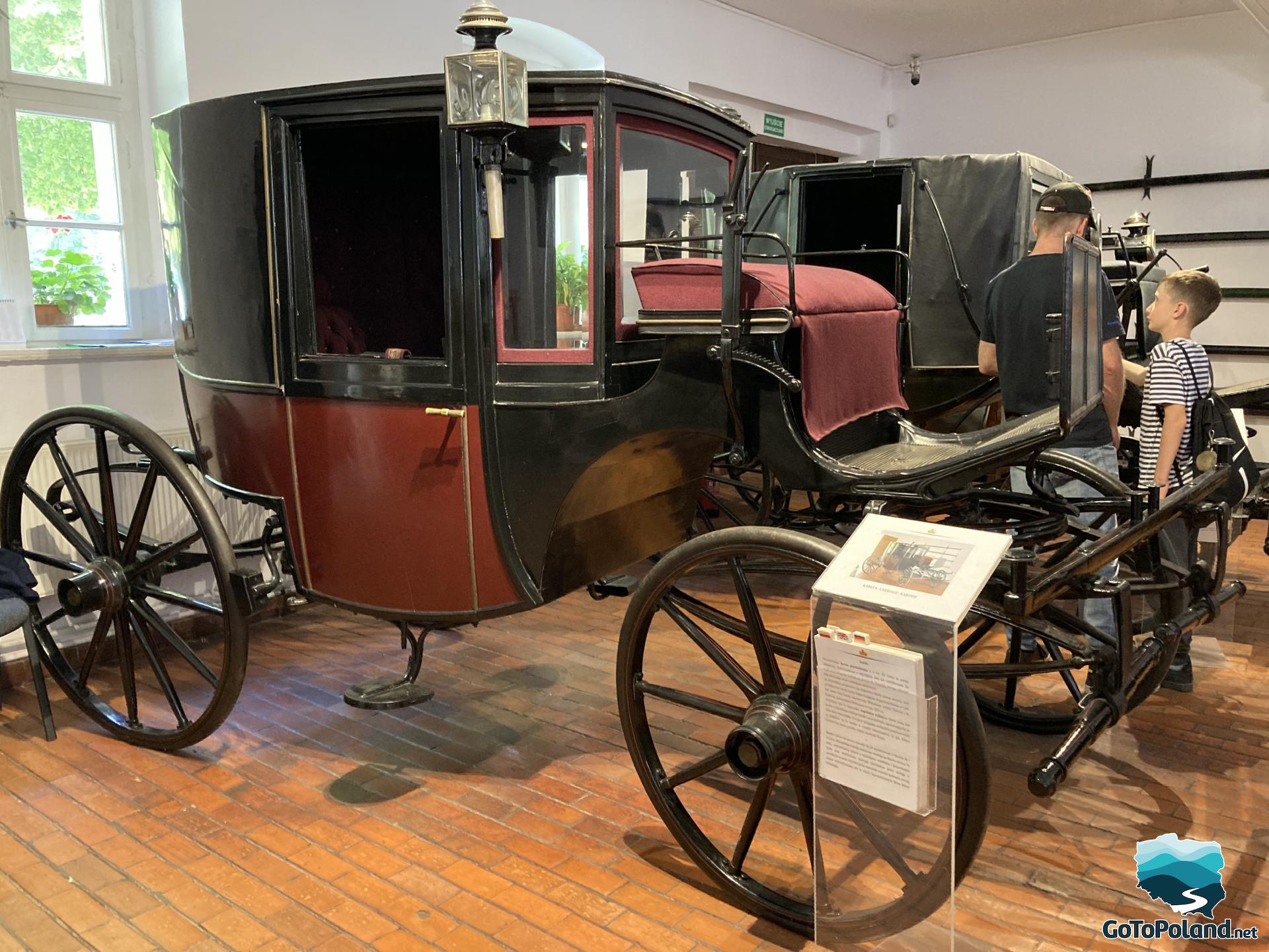 a boy and a man are standing between two old carriages 