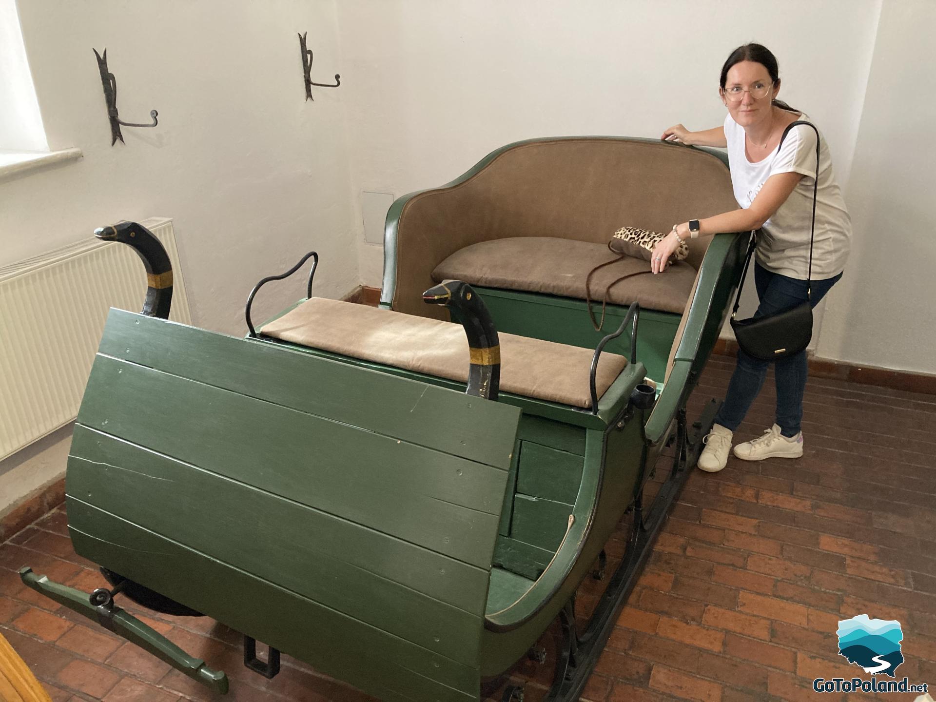 a woman is standing next to green, wooden, vintage sleigh