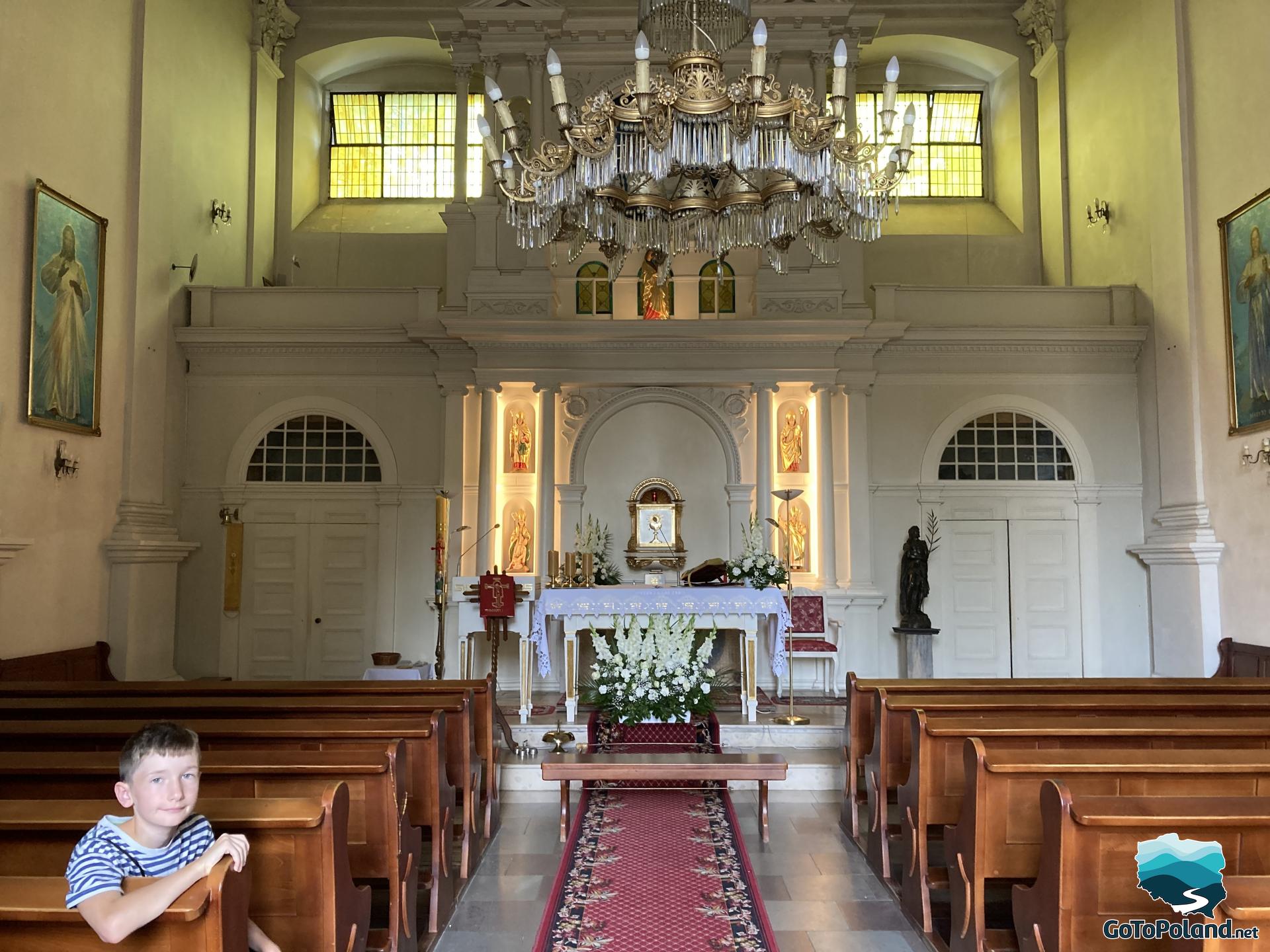 a boy is sitting inside the church, There are rows of wooden pews and white altar