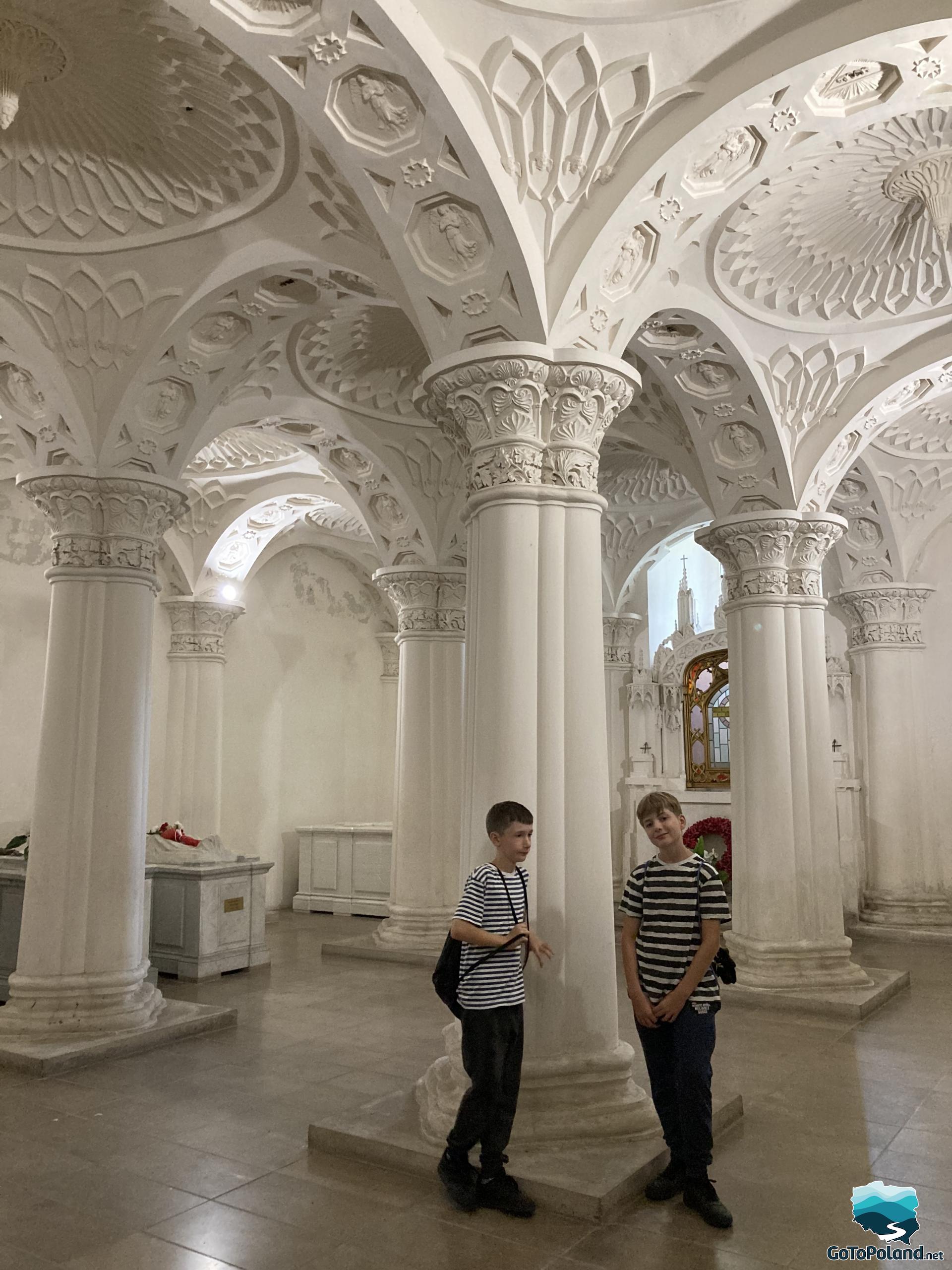 two boys are in the mausoleum and are standing next to one of the columns 