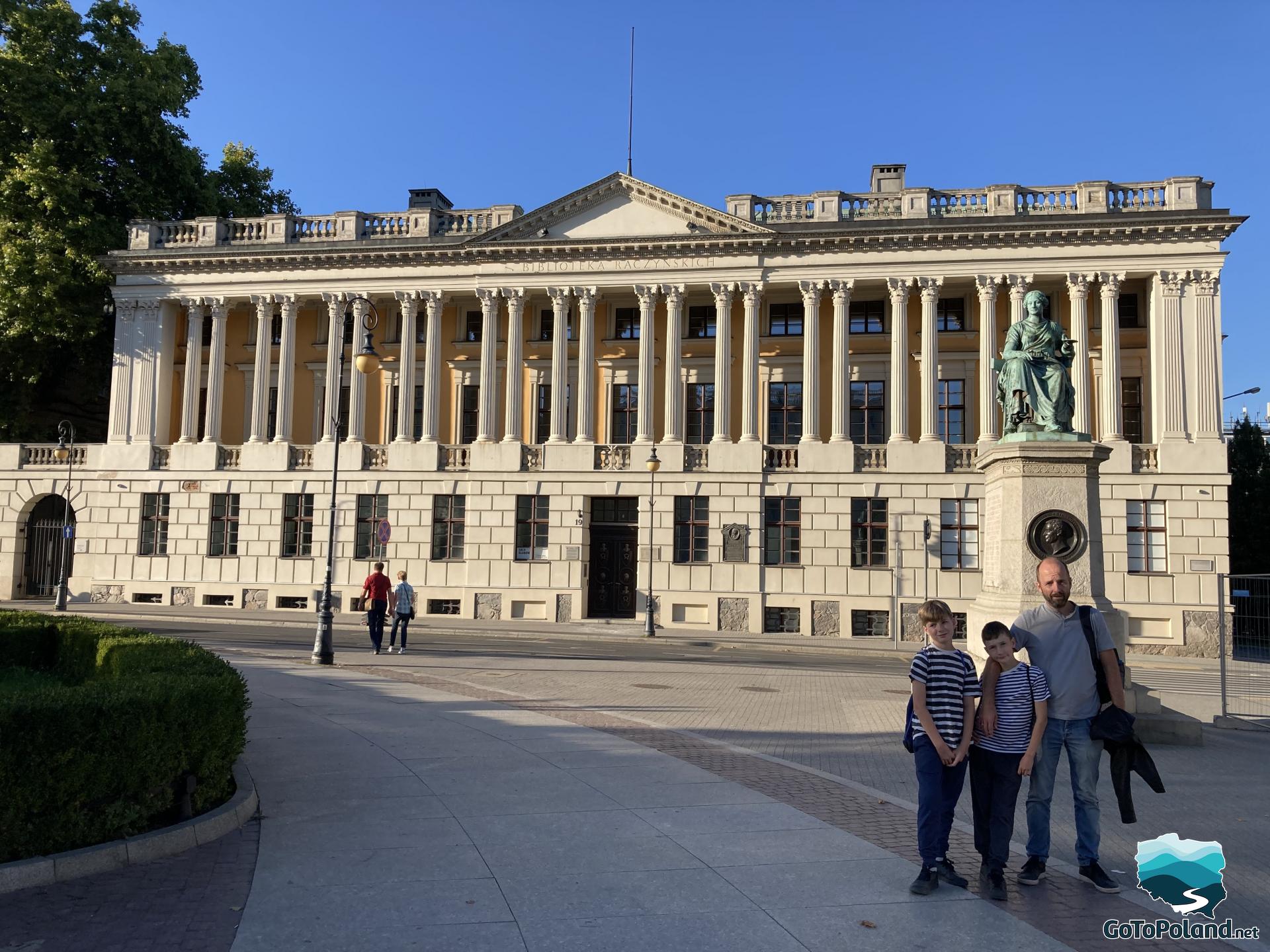two boys and a man posing in front of a neoclassical style building