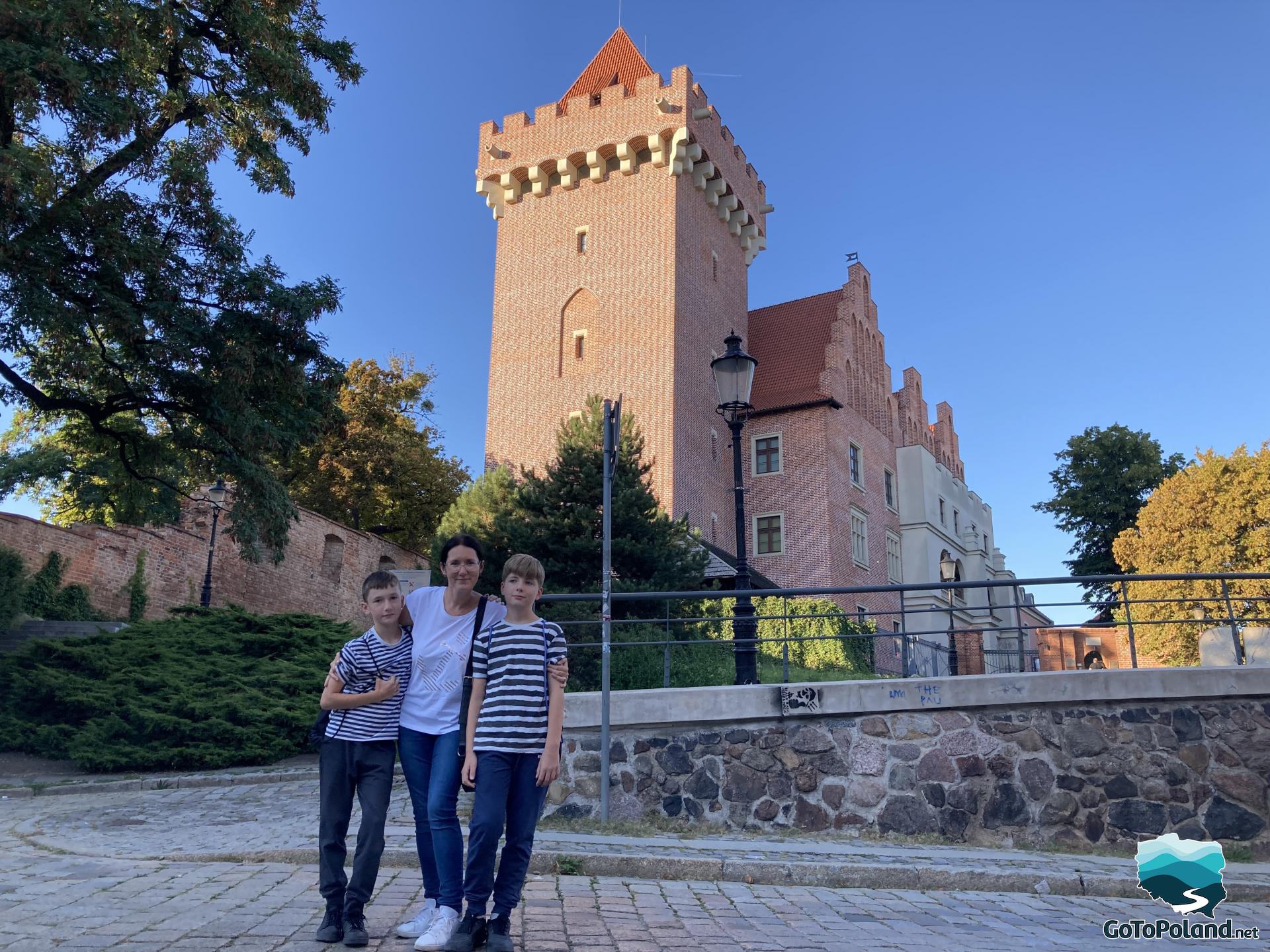 A woman and two boys are posing for a photo, behind them is a tower belonging to a former castle