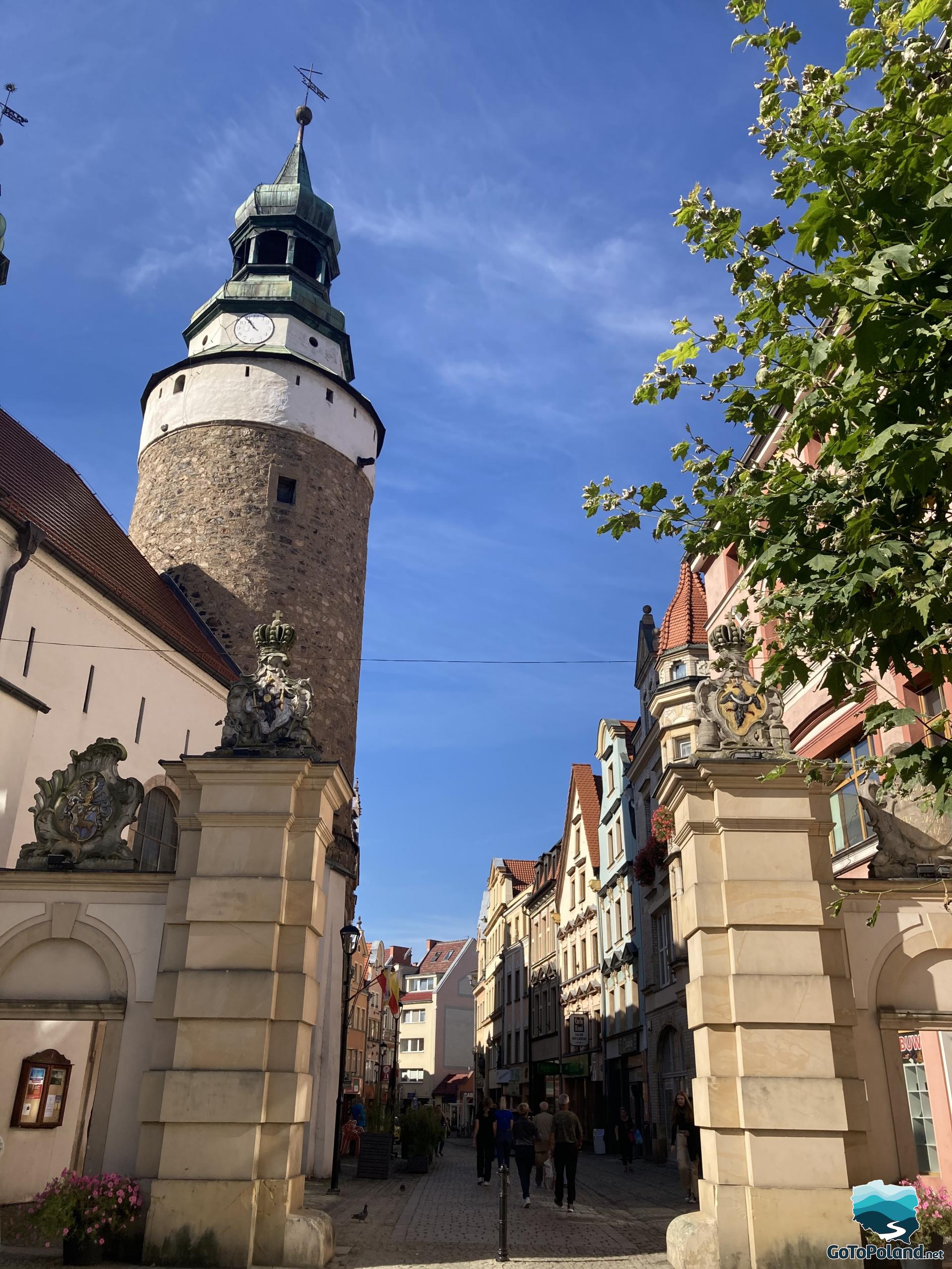 gate on which there are cartouches, on the left, behind the gate a round tower, and tenement houses in the background