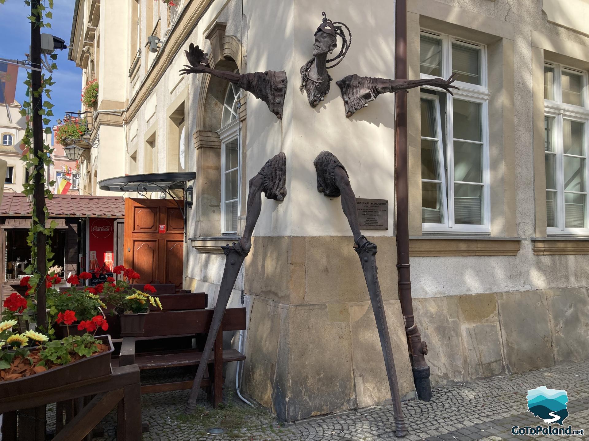 A statue of a stilt walker emerging from the corner of the building