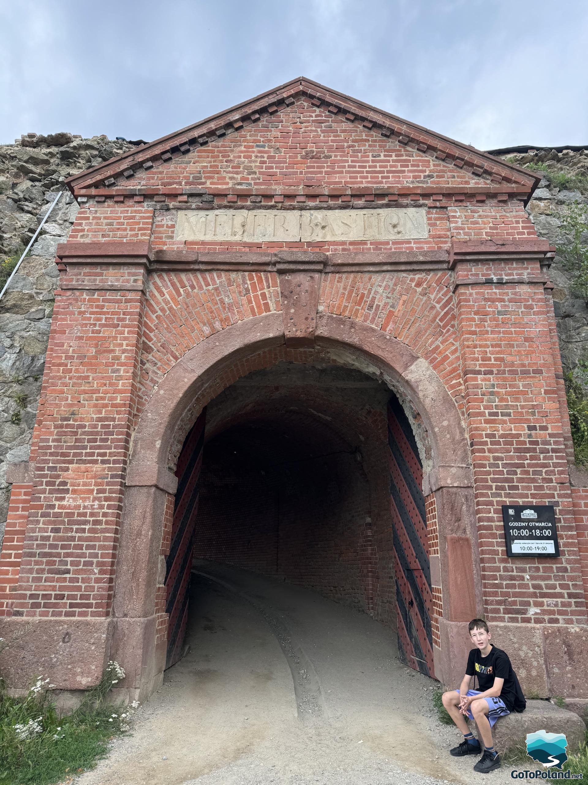 a boy is sitting on a stone next to the fortress entrance