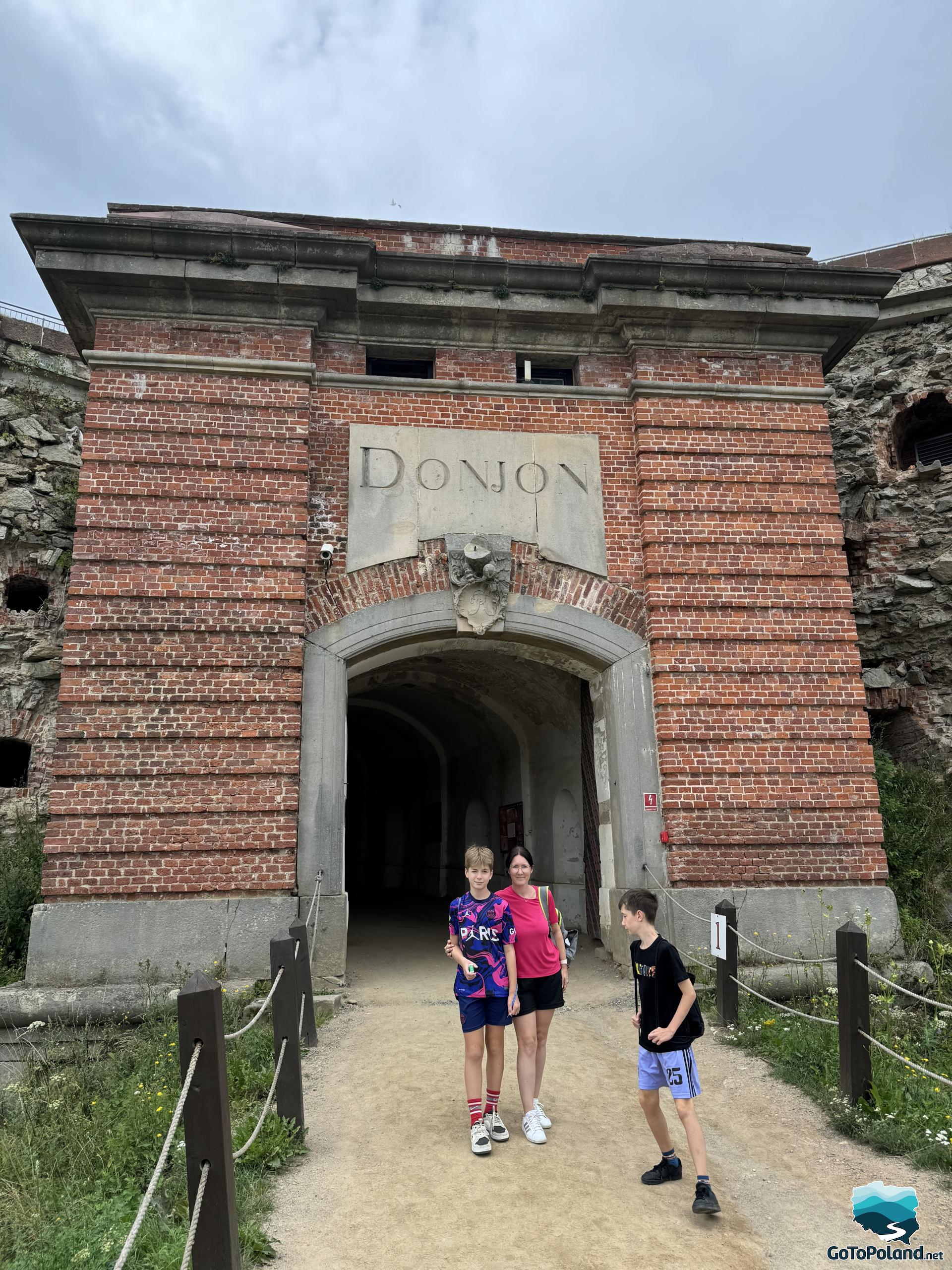 a woman and two boys are standing in front of the donjon gate