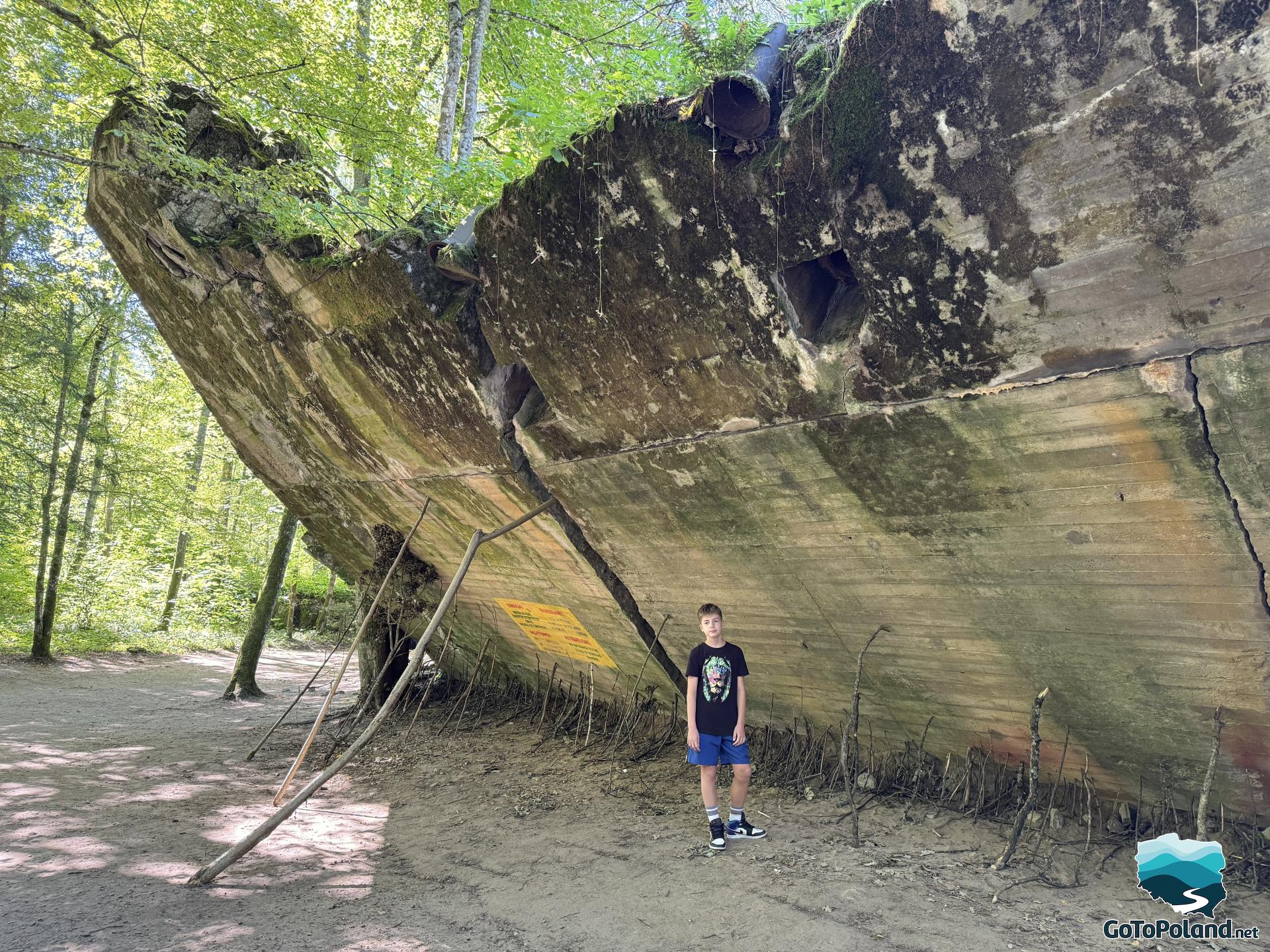 a boy is standing under the huge leaning wall
