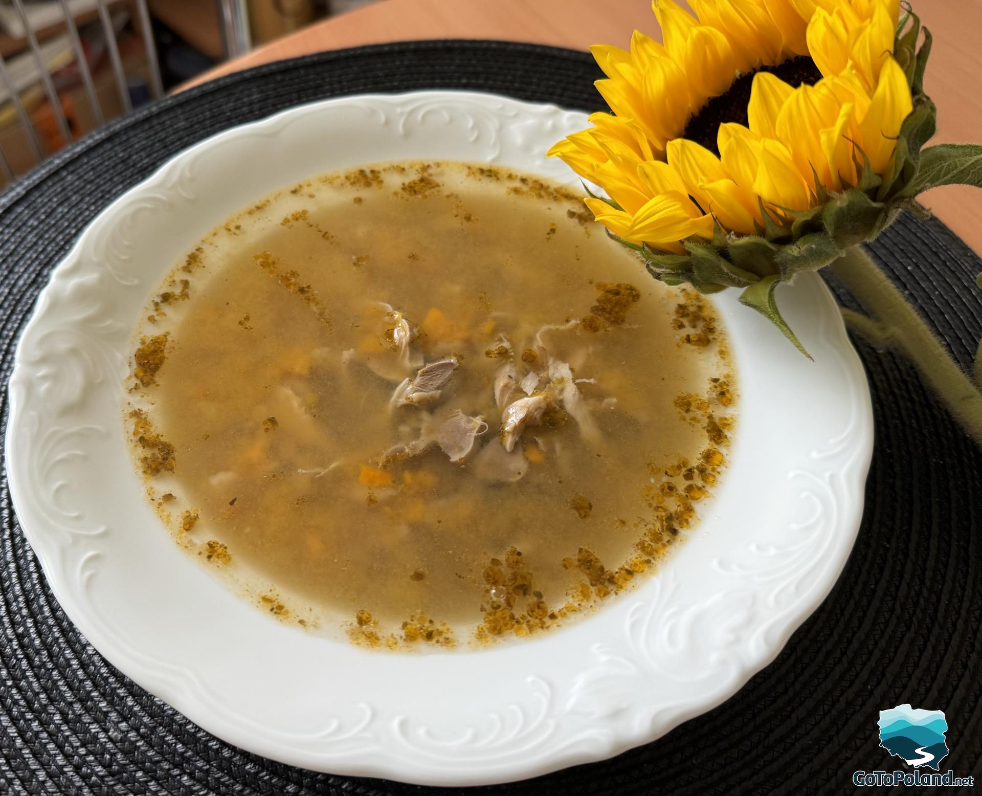 soup in a white plate, next to the plate is a sunflower for decoration 