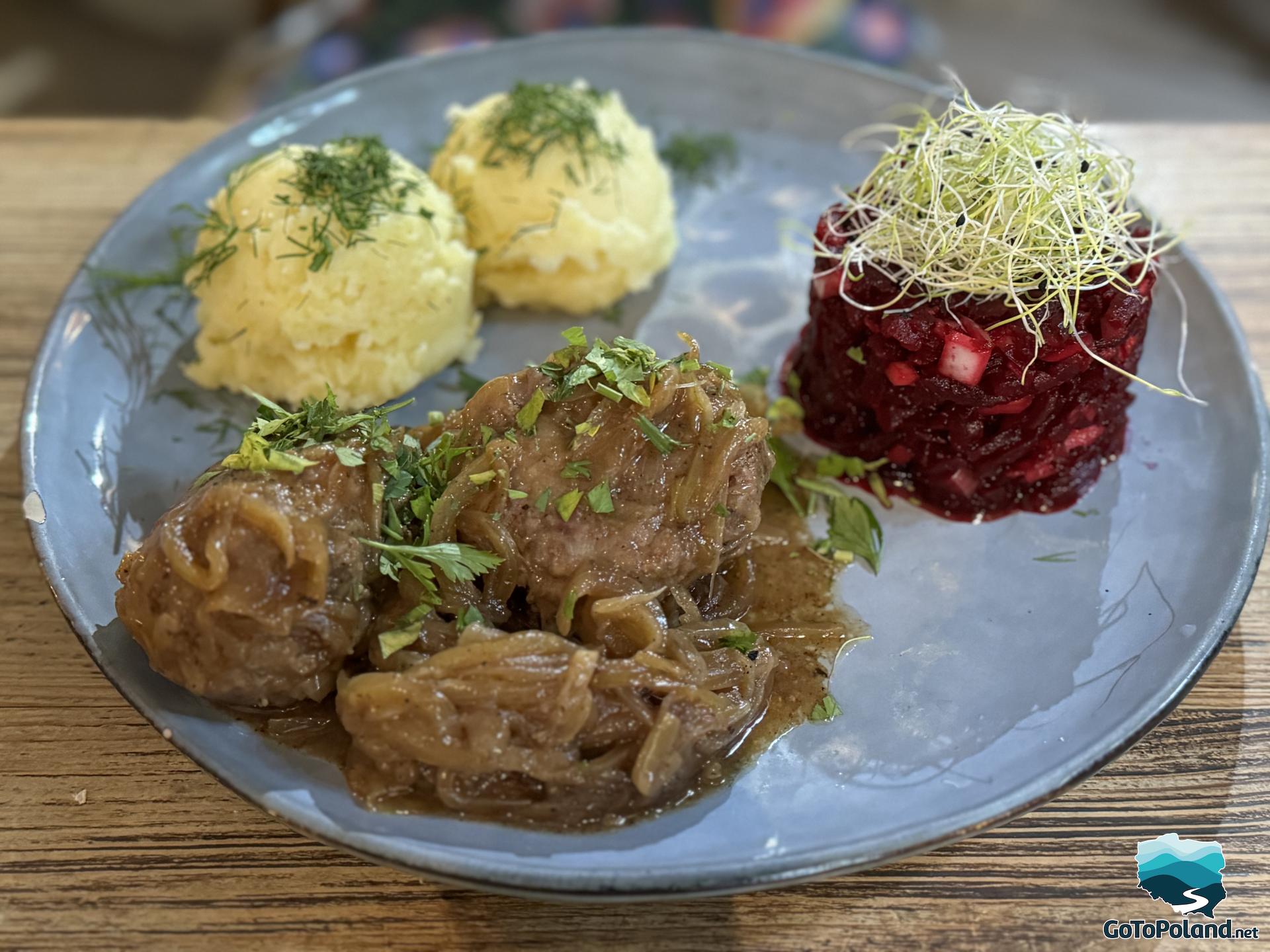 on a blue plate two balls of mashed potatoes, meat in brown sauce with fried onion and beetroot