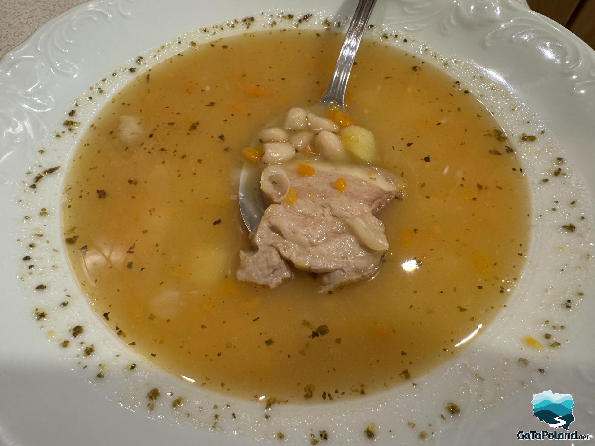 bean soup with bacon on a spoon in a white plate