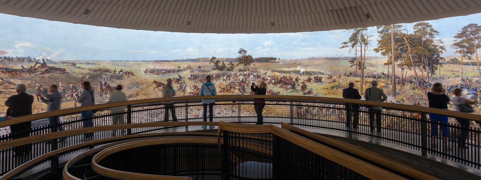 the round painting shows a battle from the 18th century, some of the fighters are on horseback, some on foot, in front of it there are spectators