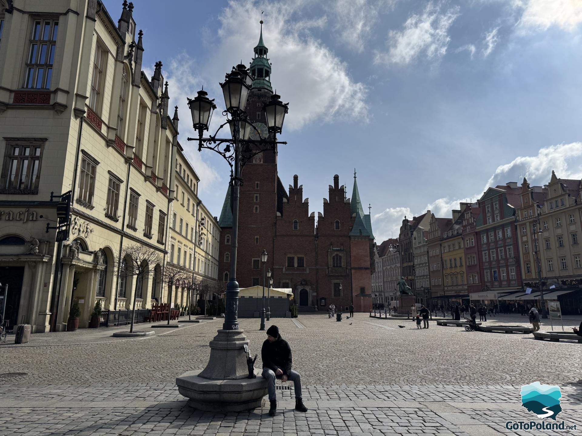 a man sitting under an antique lamppost, behind him an antique building and a city hall