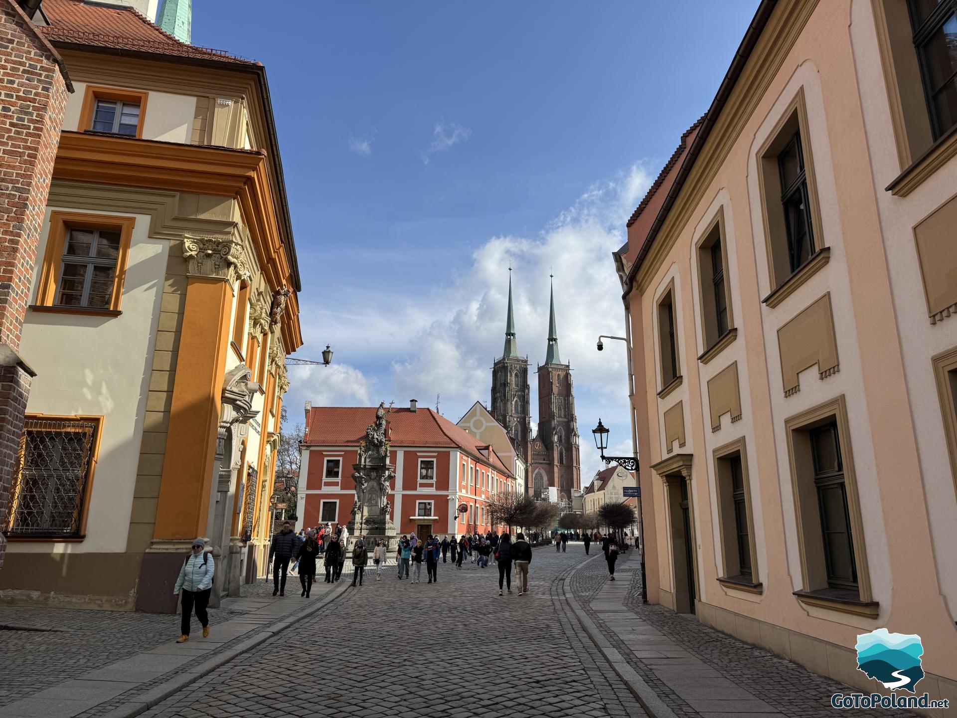 a cobbled street with colorful tenement houses on both sides and the church towers looming in the background
