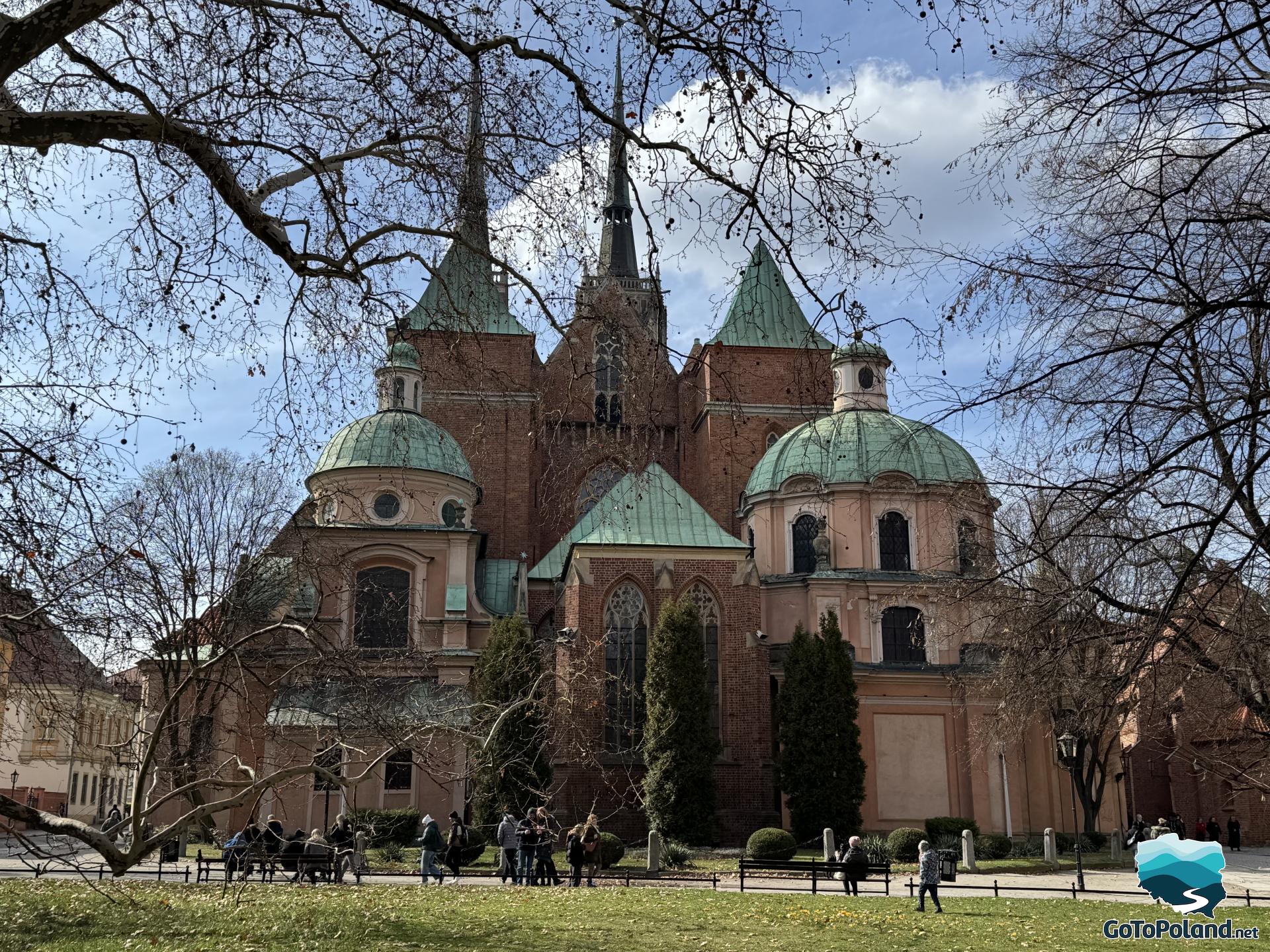 benches on which people sit, behind them a cathedral with two towers and two round domes