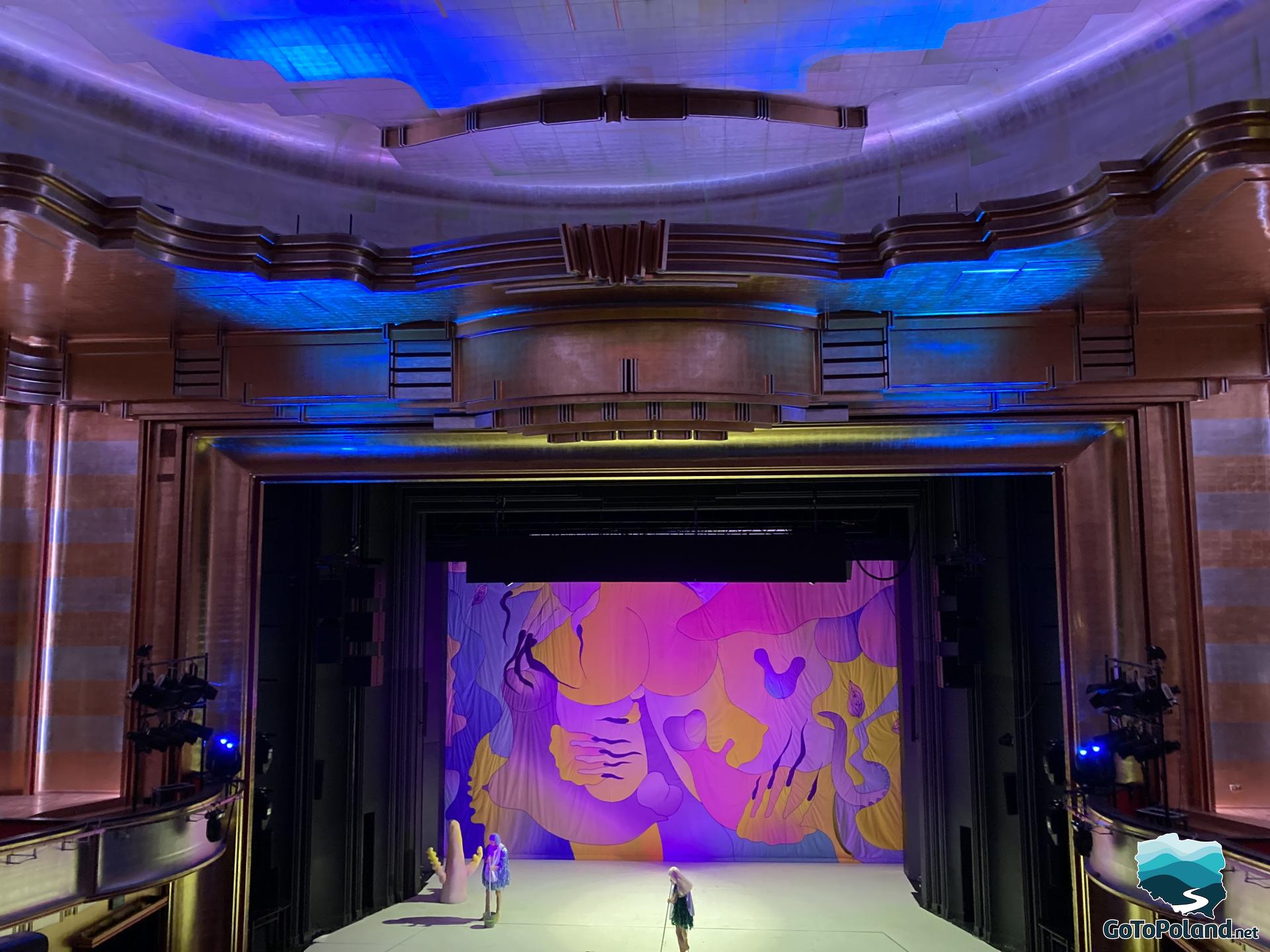 visible stage in the theater, lit in pink, on the stage 2 actresses with brooms