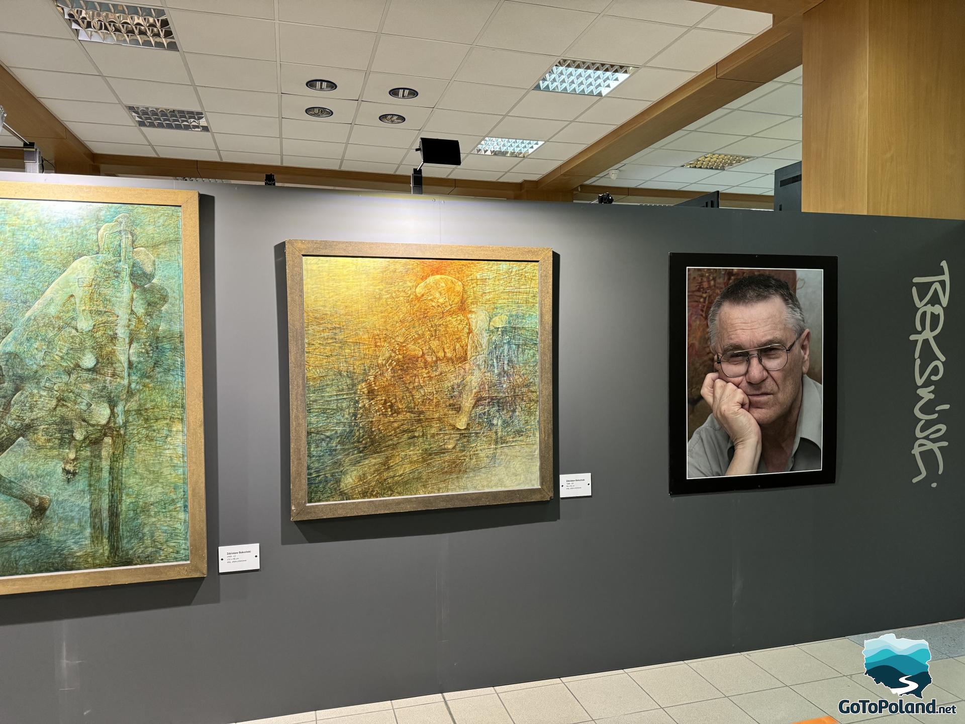 there are 2 paintings and a portrait of their creator hanging on the wall