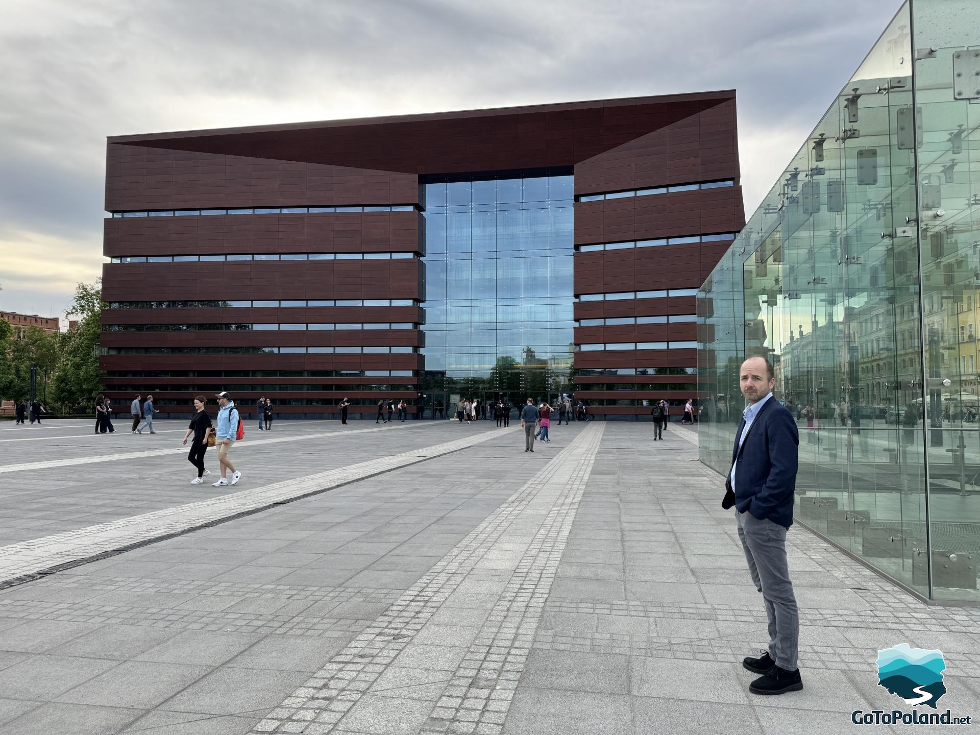 a man stands in a square in front of a large brown and glass building