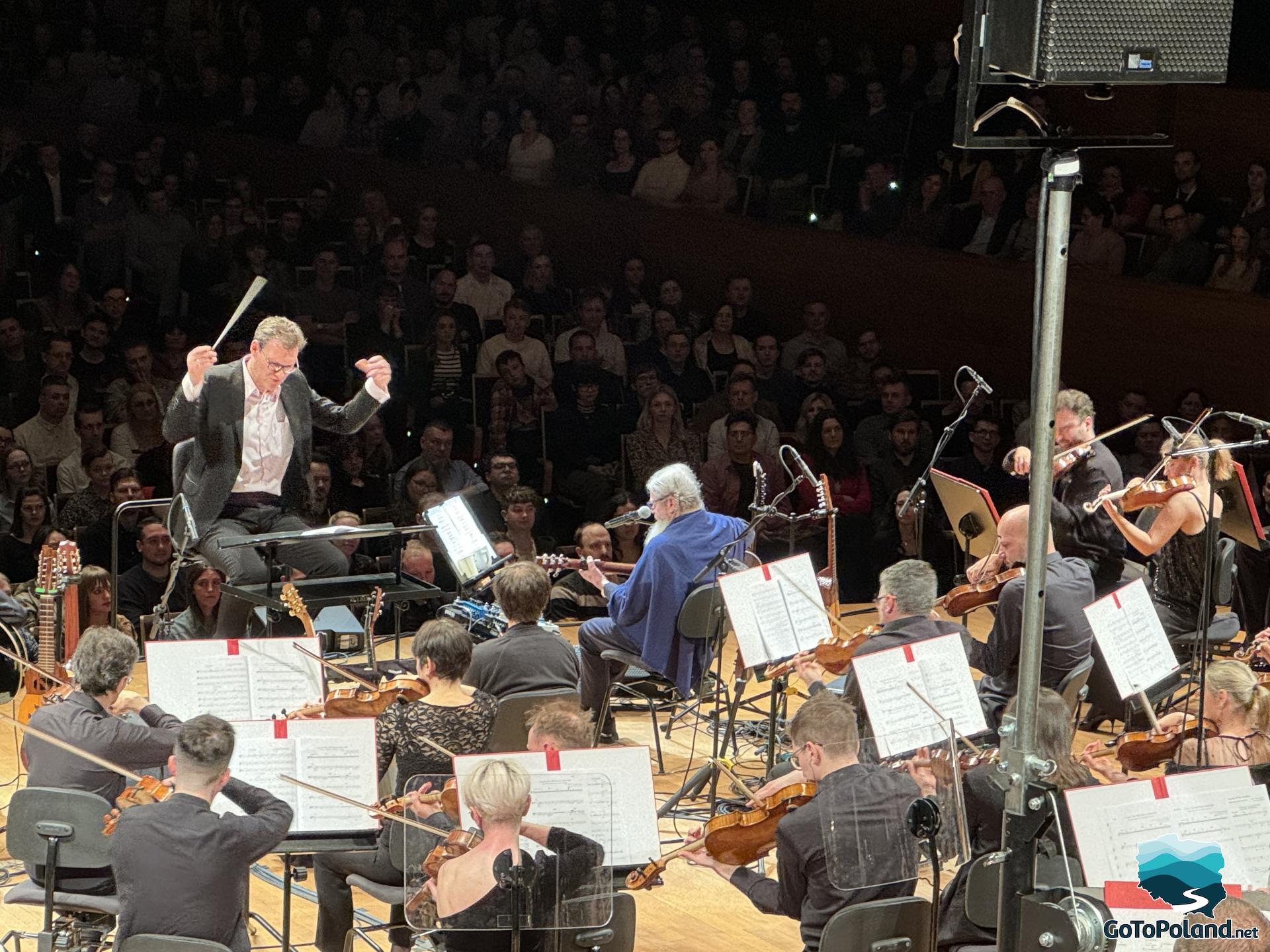 the stage, with the conductor and the entire orchestra on it, and the spectators in the background
