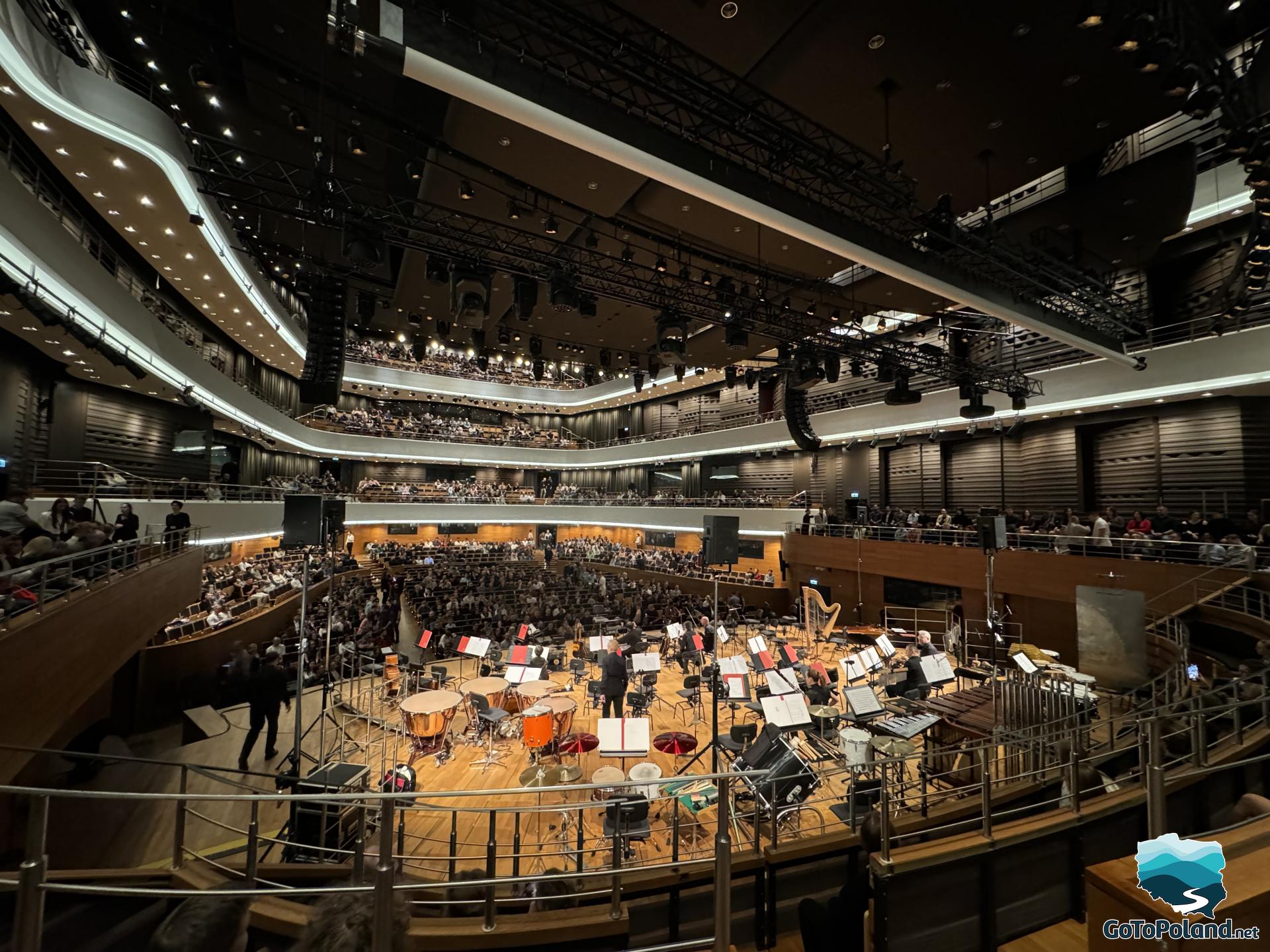 the stage has musical instruments on it, the audience sits around the stage and waits for the concert