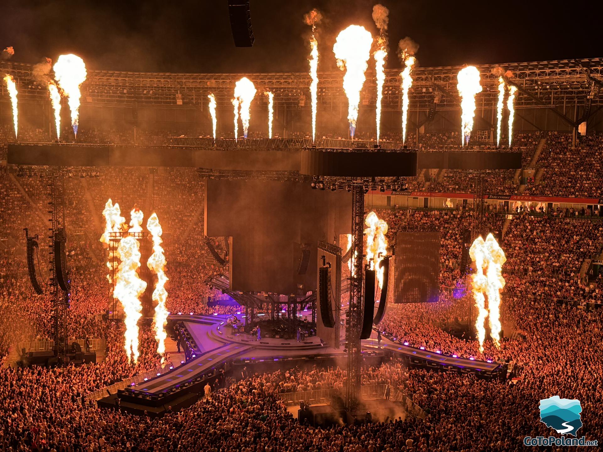 stadium full of fans, stage in the middle, fireworks from the fire around the stage
