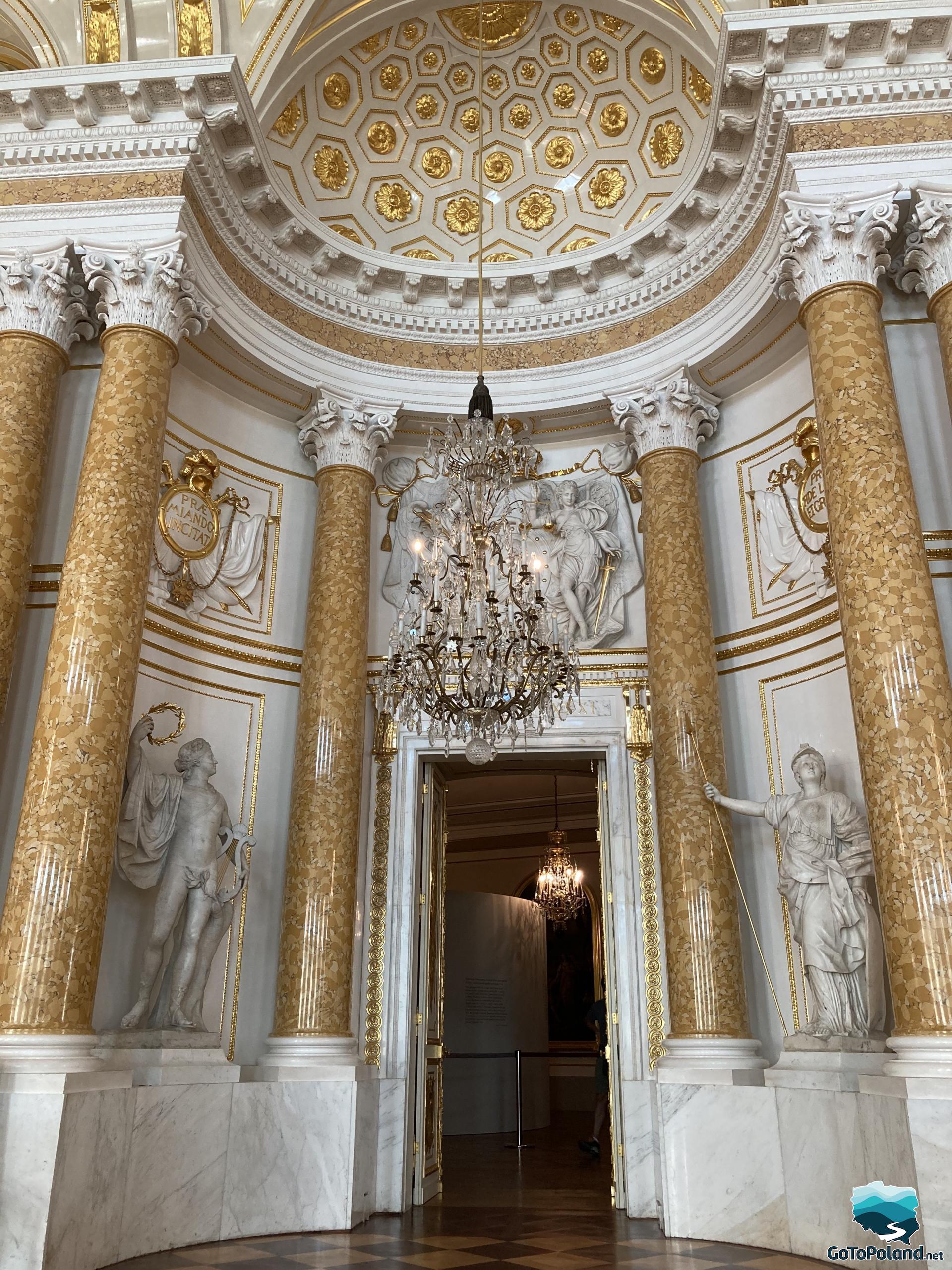 the main entrance to the ceremonial ballroom in the castle, crystal chandelier, yellow columns with Corinthian capitals and Roman style sculptures on both sides of the entrance
