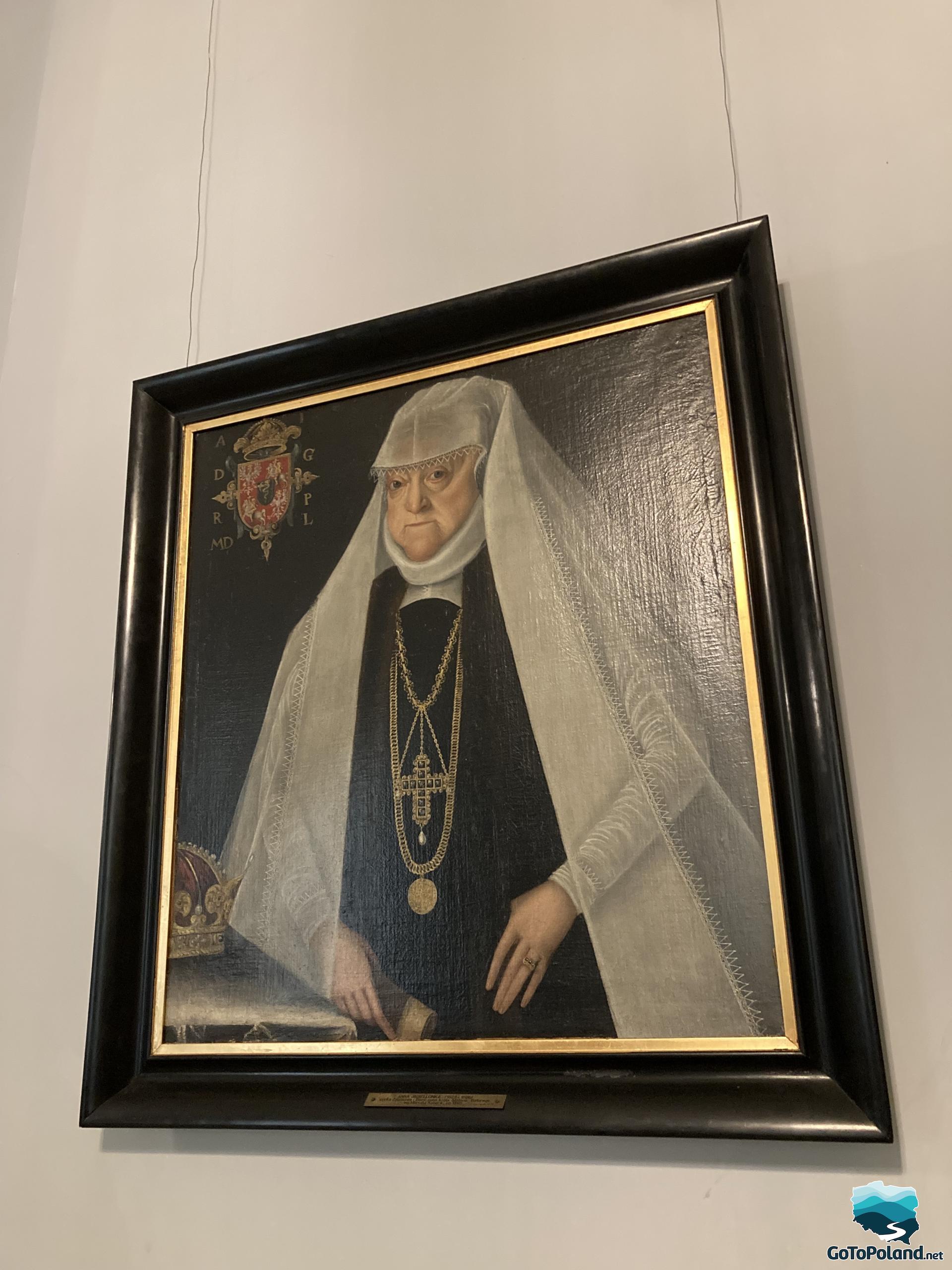 the hanging portrait shows a woman in a black dress with gold chains and a cross, the woman has a long white scarf covering her head, arms down to her legs. There is a crown on the side of the saddle. this woman is Anna Jagielonka, queen of Poland in the 16th century