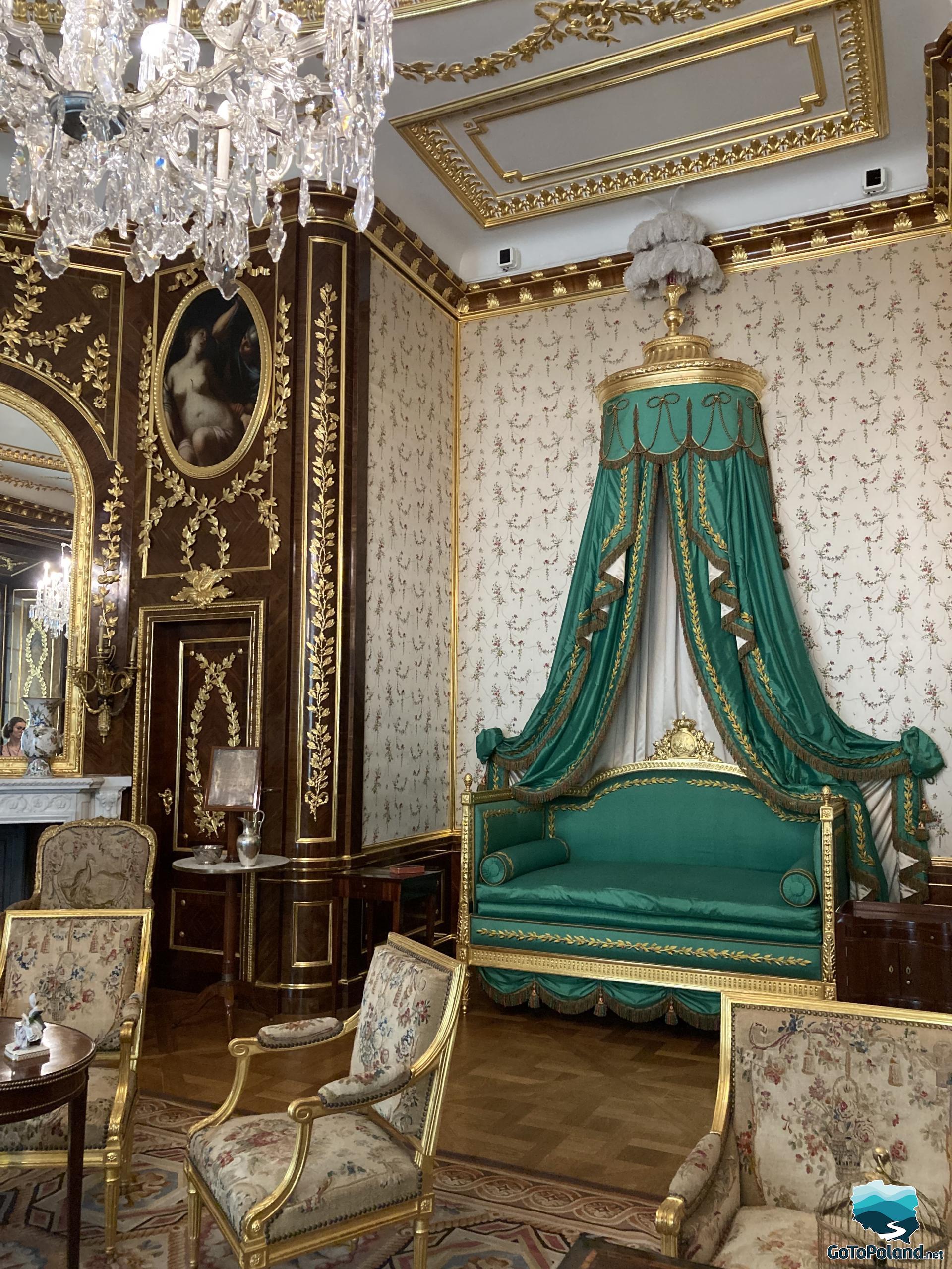 the hall is richly decorated, there is a crystal chandelier, chairs with golden backs, a mirror in a golden frame, a wall with golden leaves and a small green sofa or chaise with a green canopy