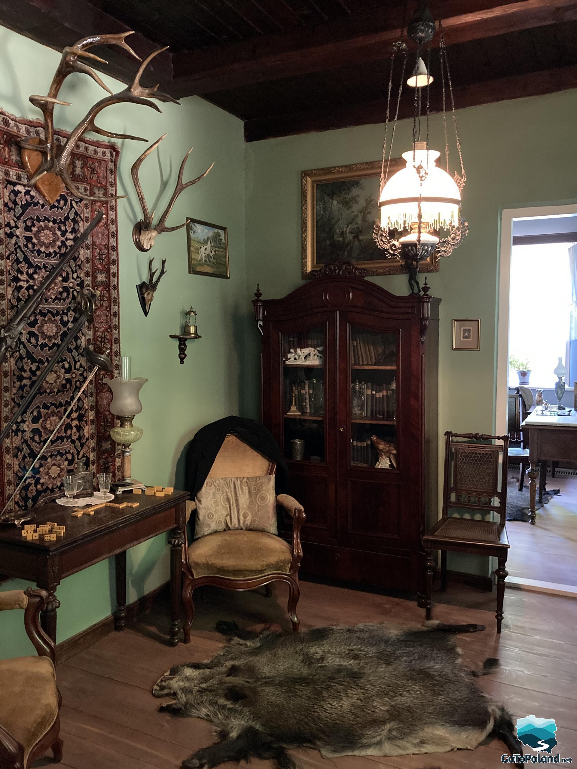 a room decorated in a hunting style, antlers hang on the wall, there is a boar skin on the floor, a lighted lamp hangs, the furniture is wooden in a dark color