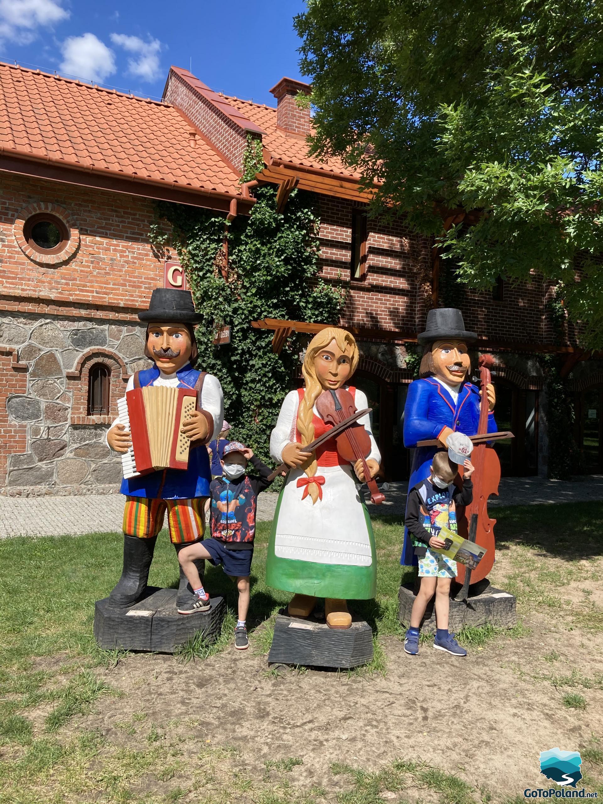 two kids are standing by wooden, colorful sculptures presenting folk figures in folk costumes