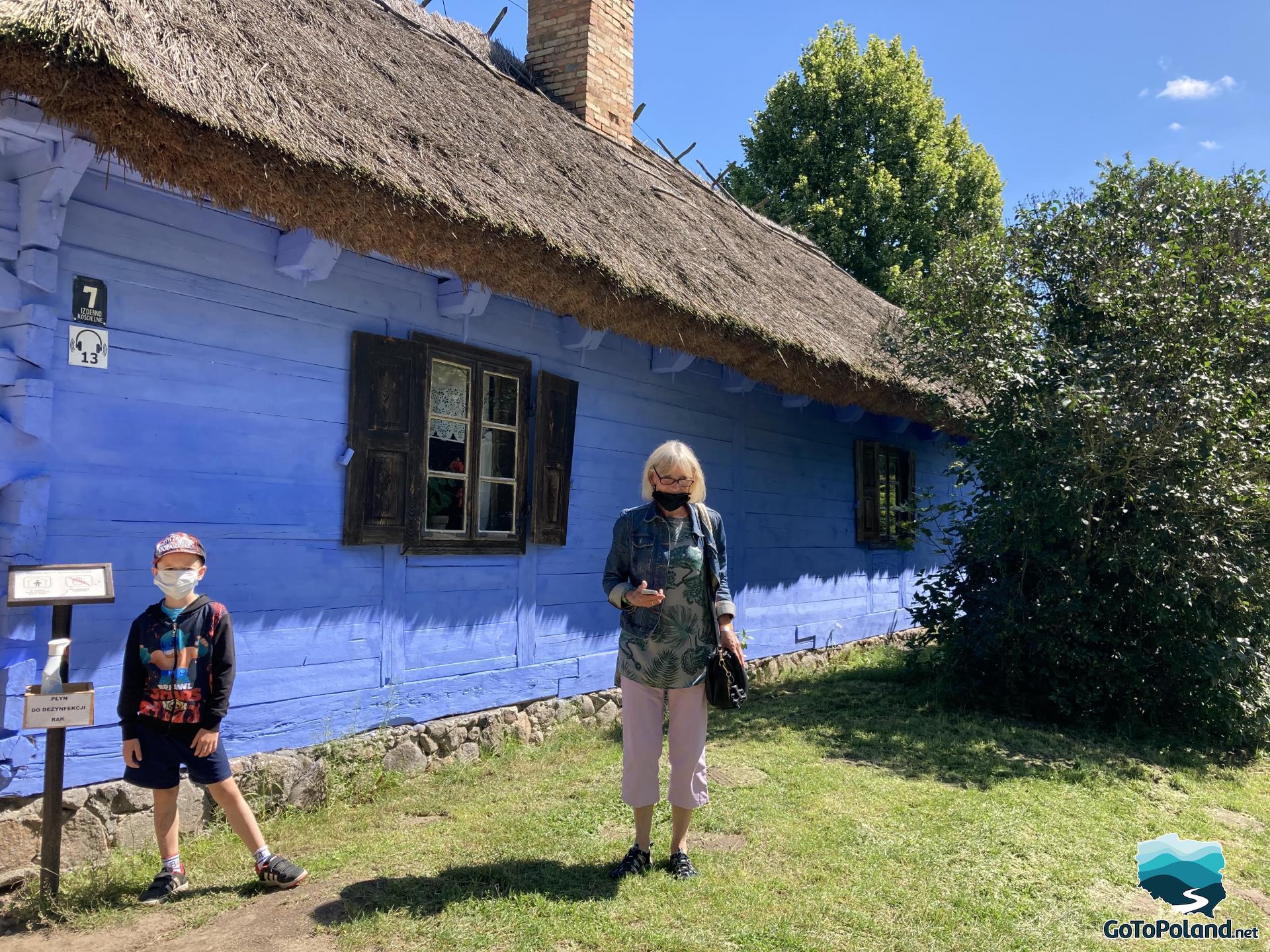 a boy and a old woman in front of blue hut