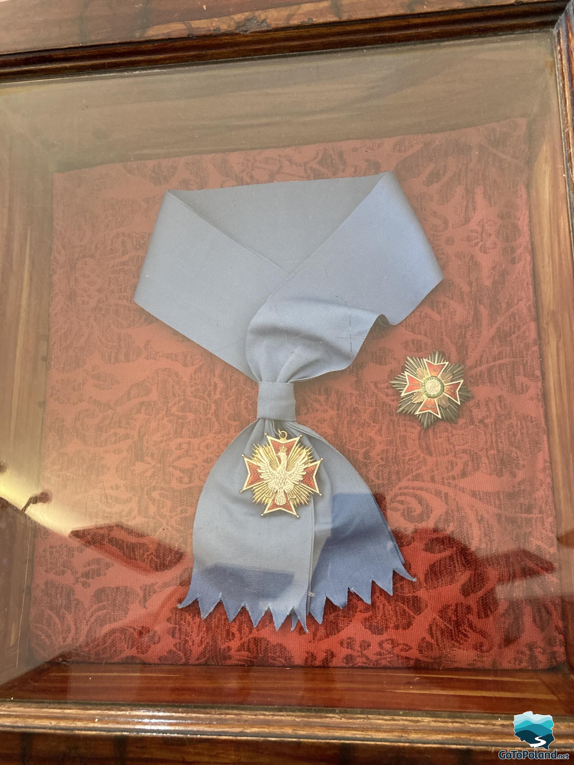 in a frame on a red fabric and a blue sash lies the Order of the White Eagle
