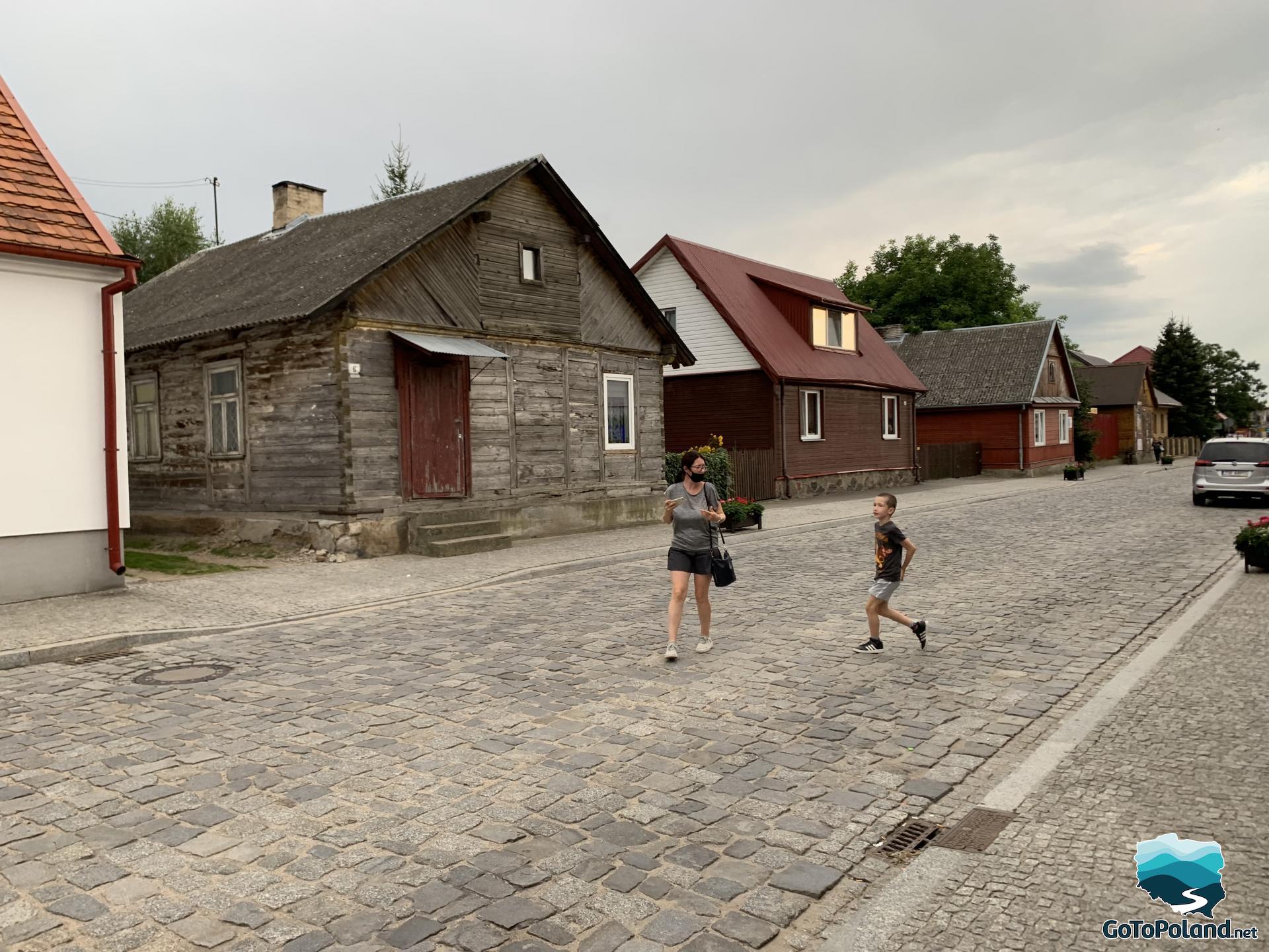 some old huts in the street, there is a woman and a boy on the cobbled street